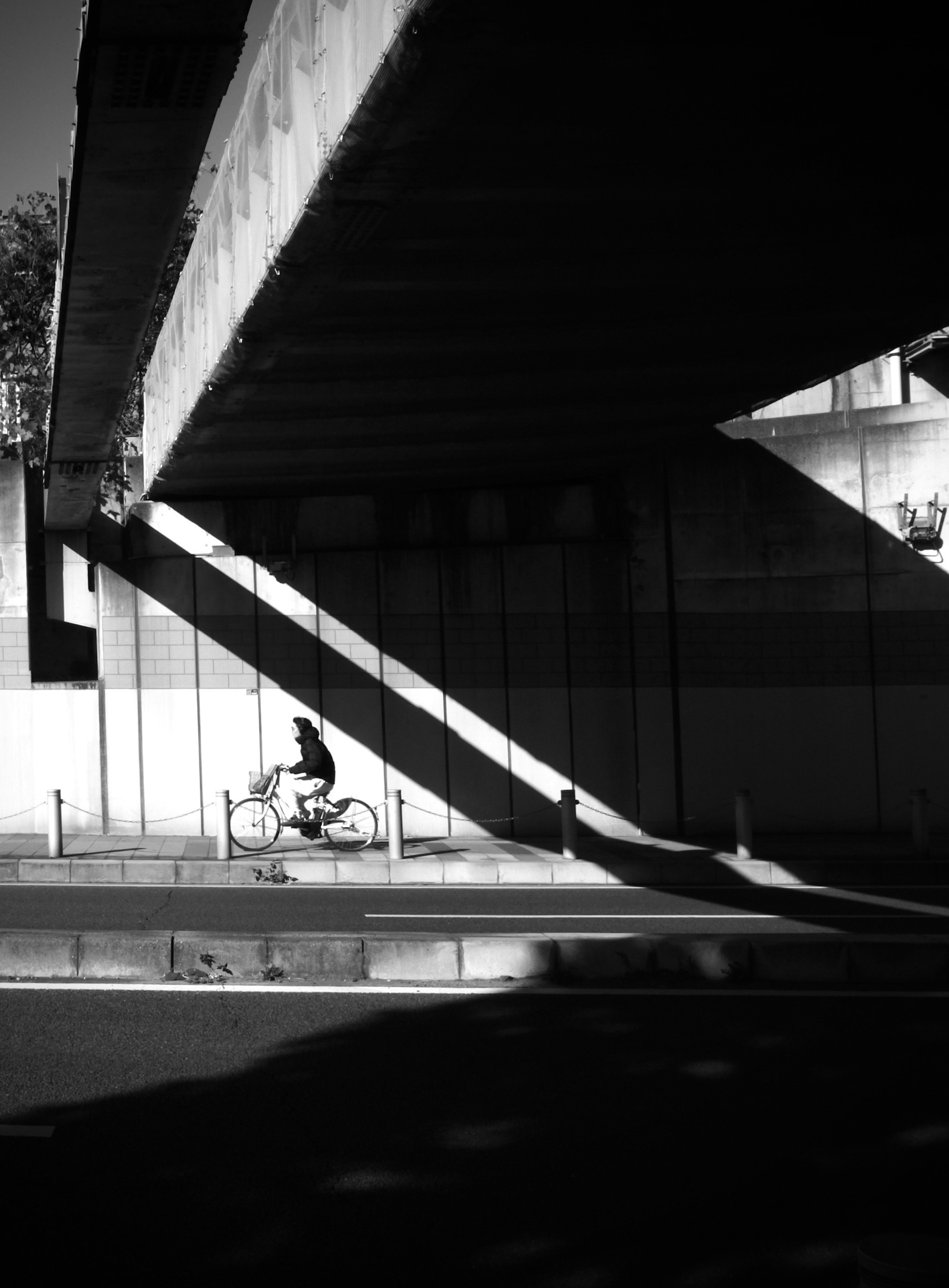 A cyclist passing under a large overpass in a black and white urban setting