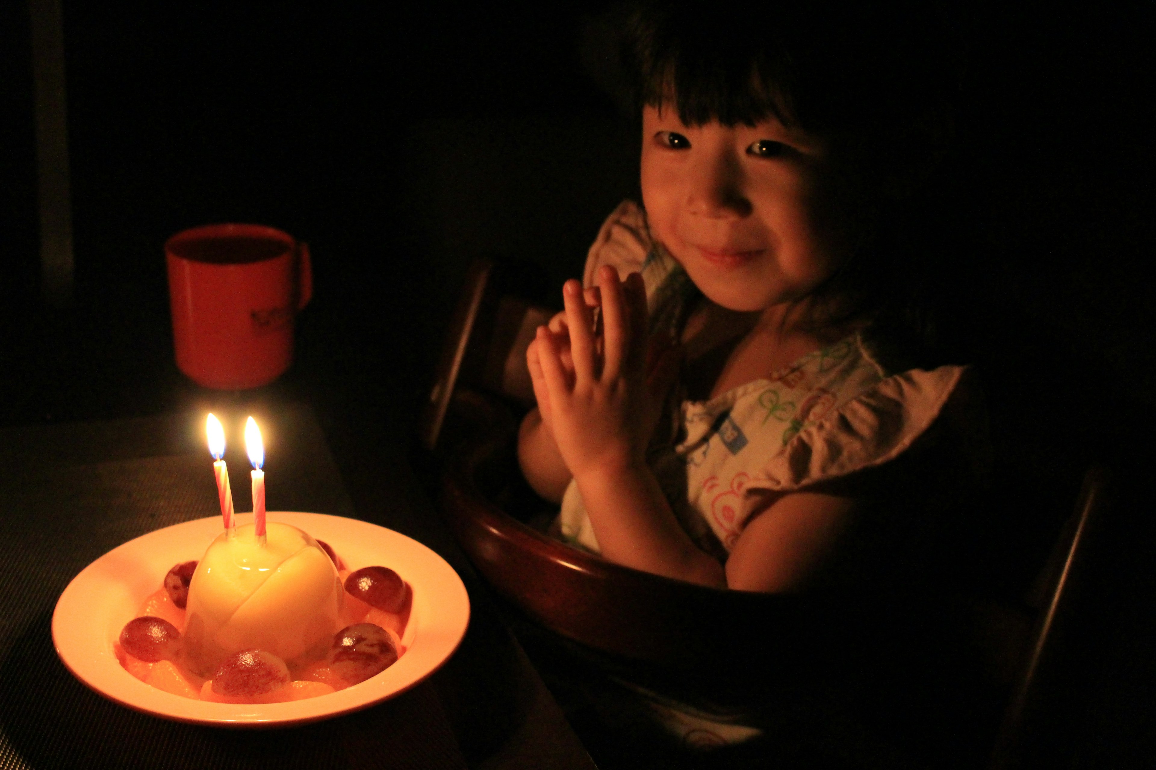 Child smiling with hands together in front of a cake in a dark setting