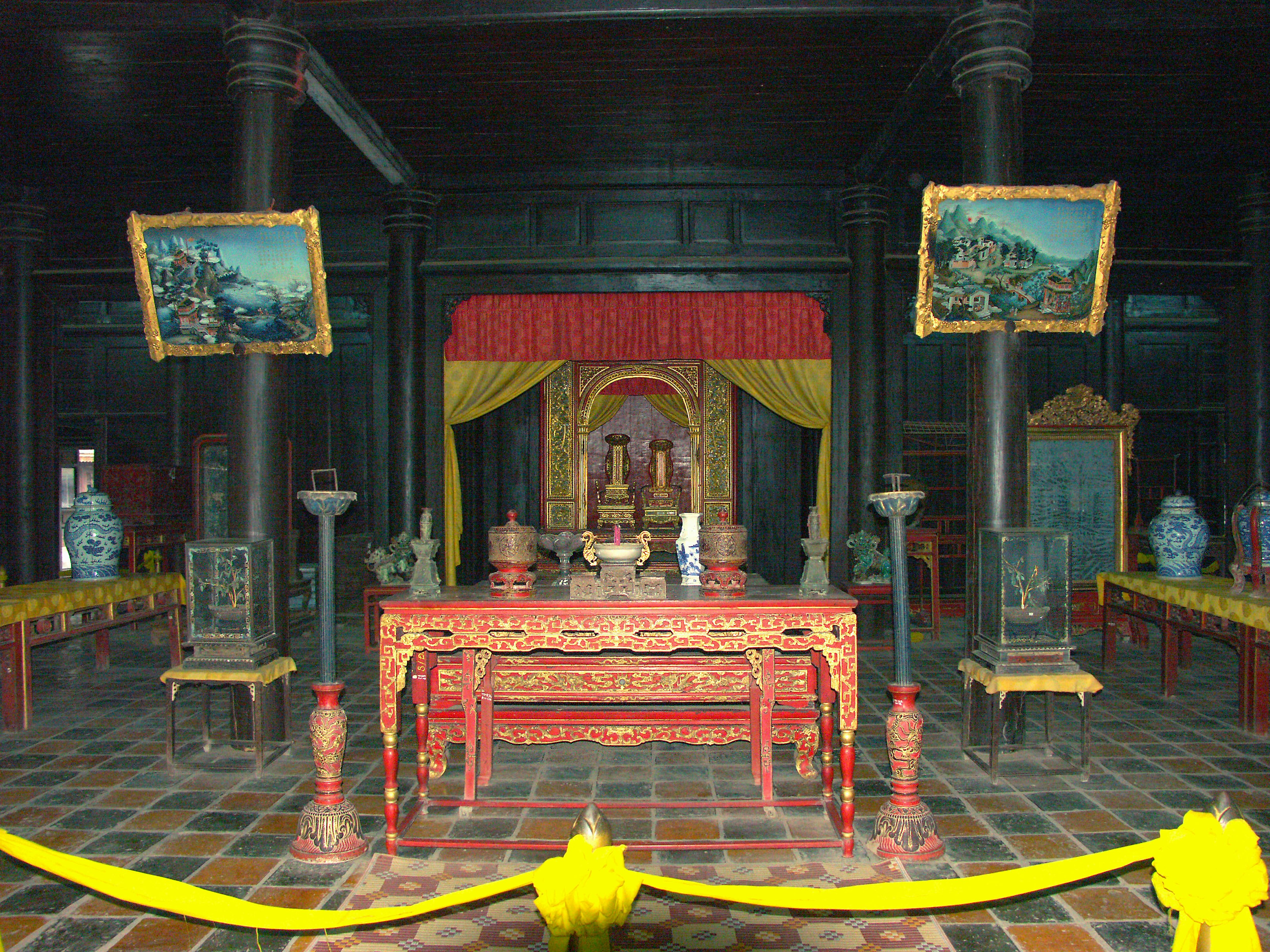 Traditional Chinese interior space with a decorated table in the center and a red curtain behind it paintings on the walls and ceramic decorations around