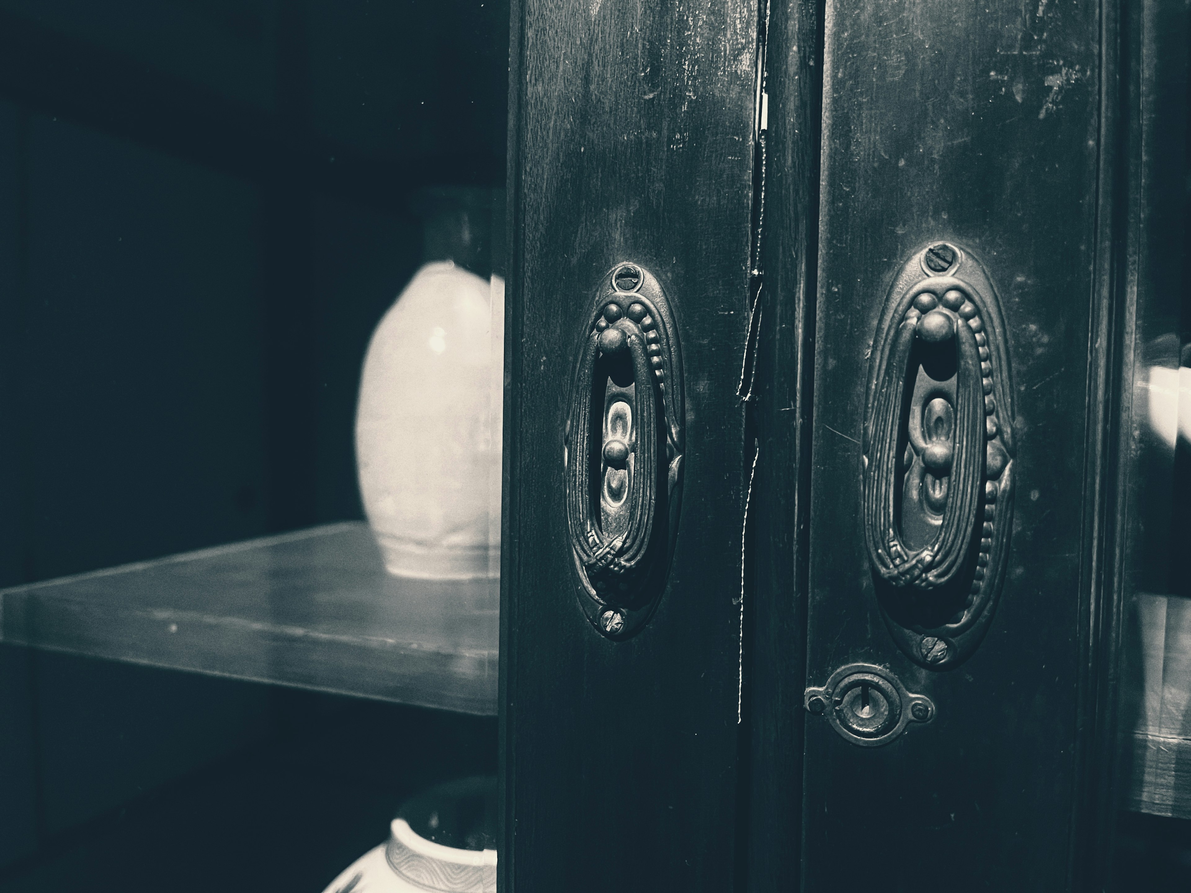 Detail of a black cabinet door with vintage handles and a ceramic vase visible