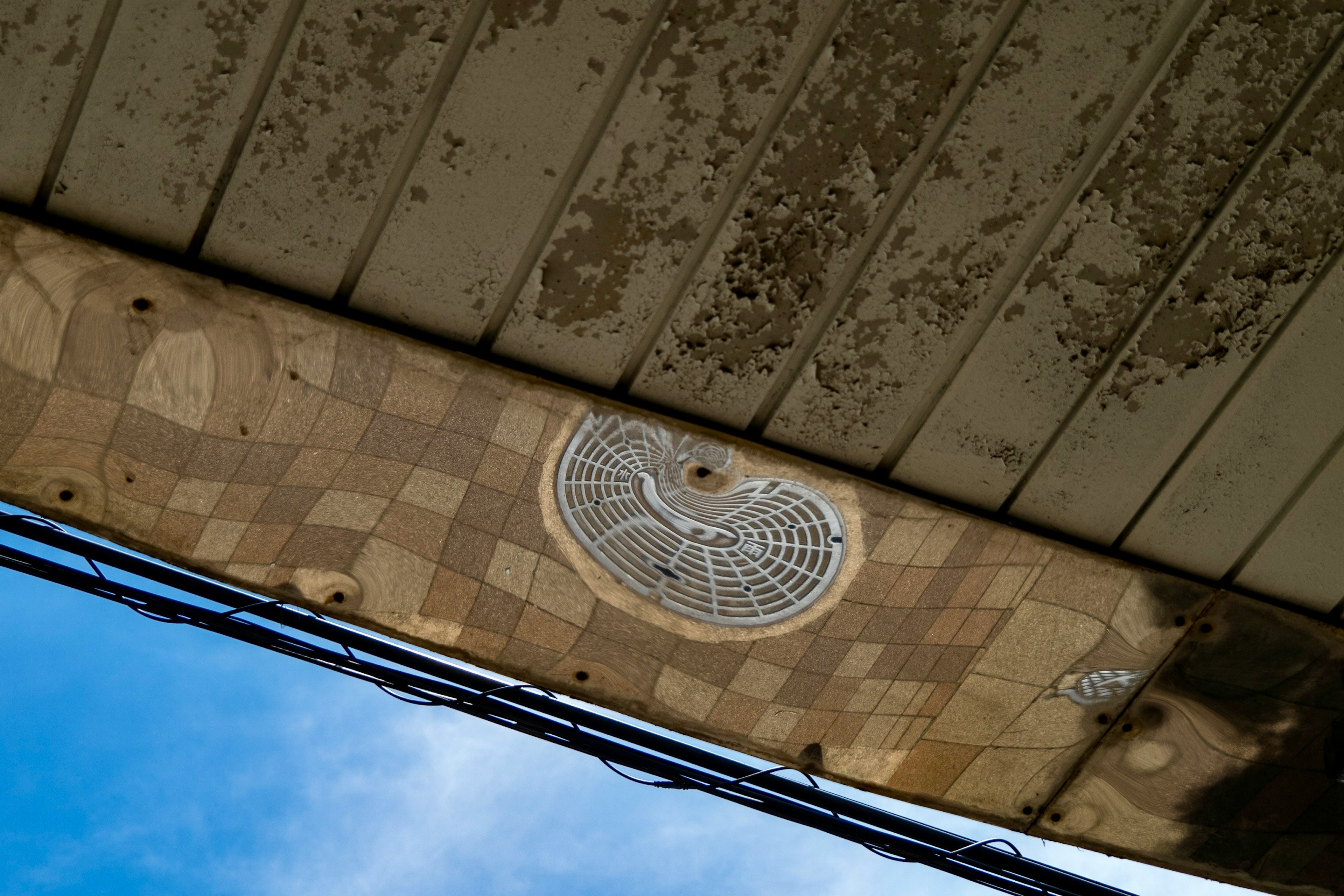 Ceiling view from underneath with a patterned surface and vent against blue sky