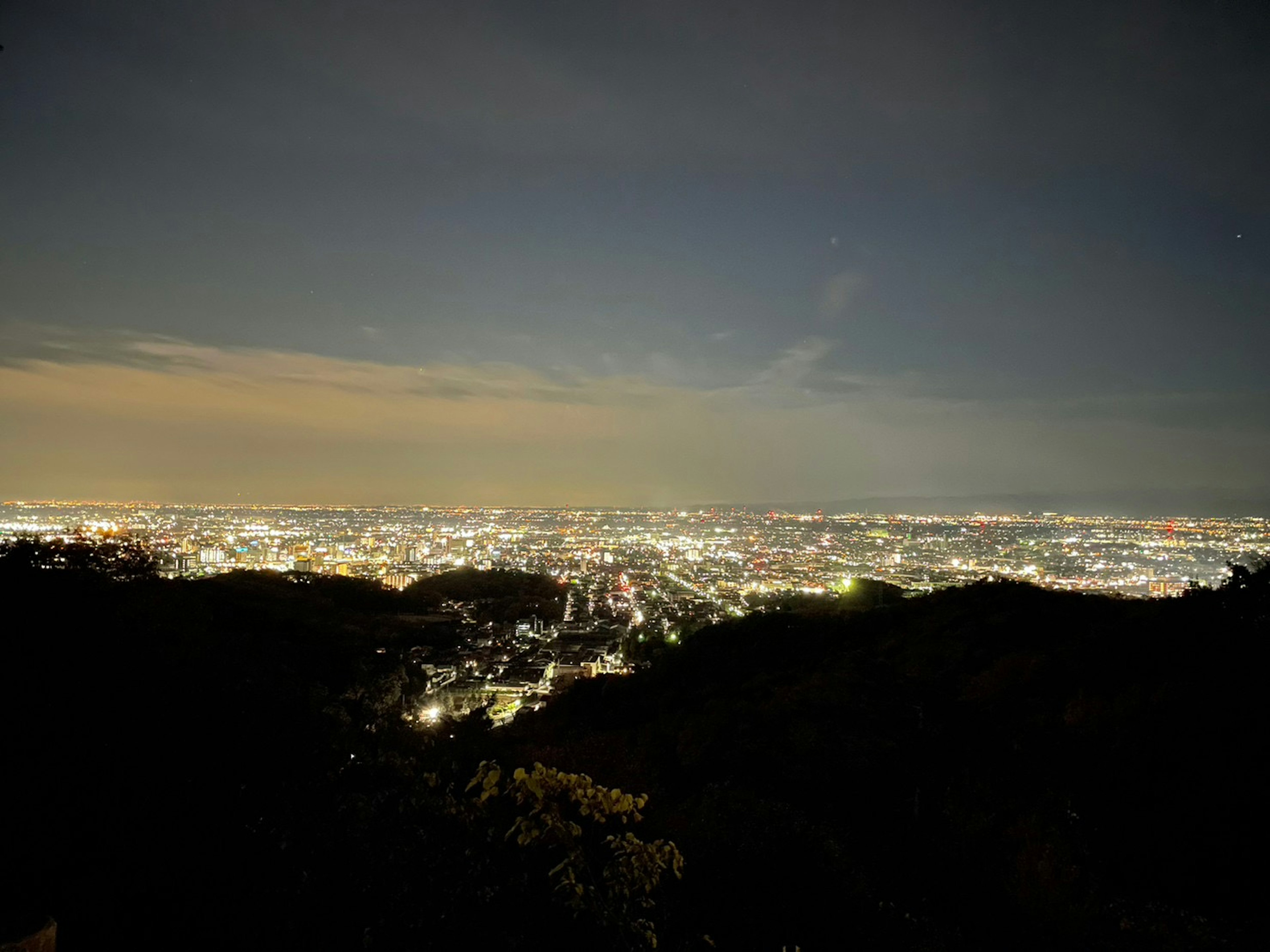 Pemandangan panoramic kota di malam hari dengan cahaya terang dan siluet gunung gelap