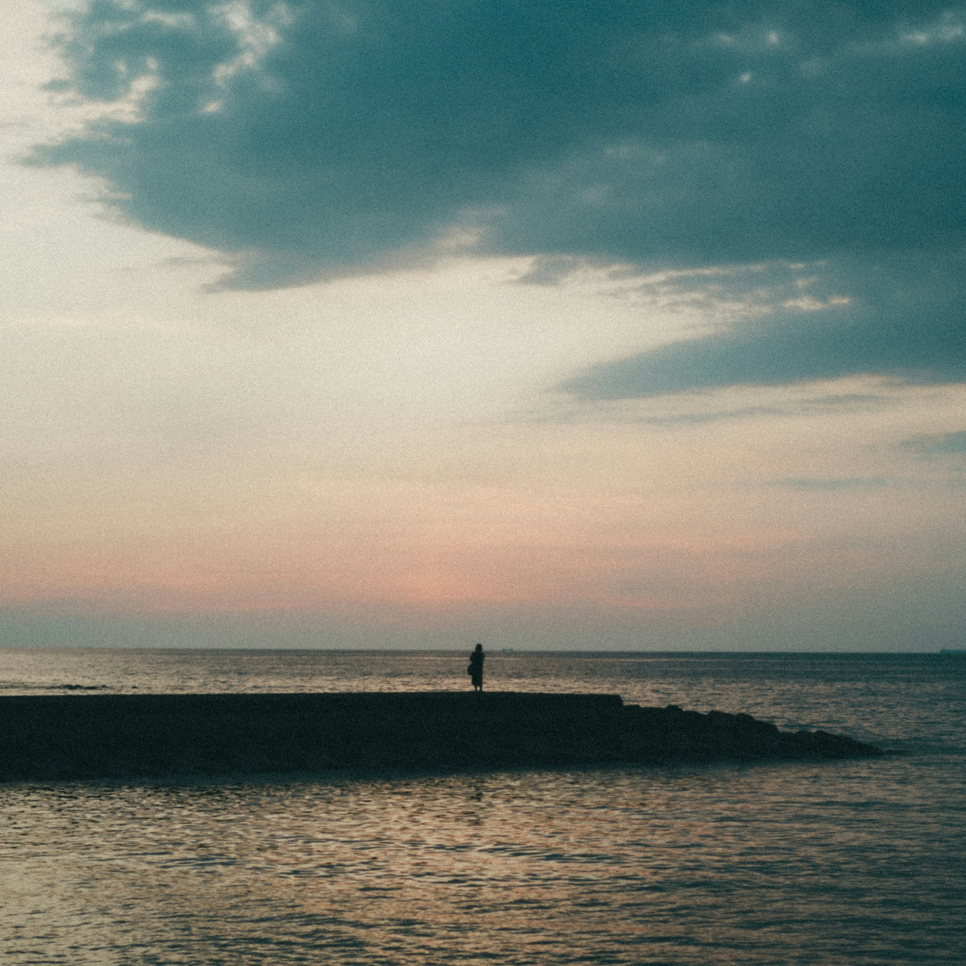 Silhouette of a person standing on a calm sea shore at sunset