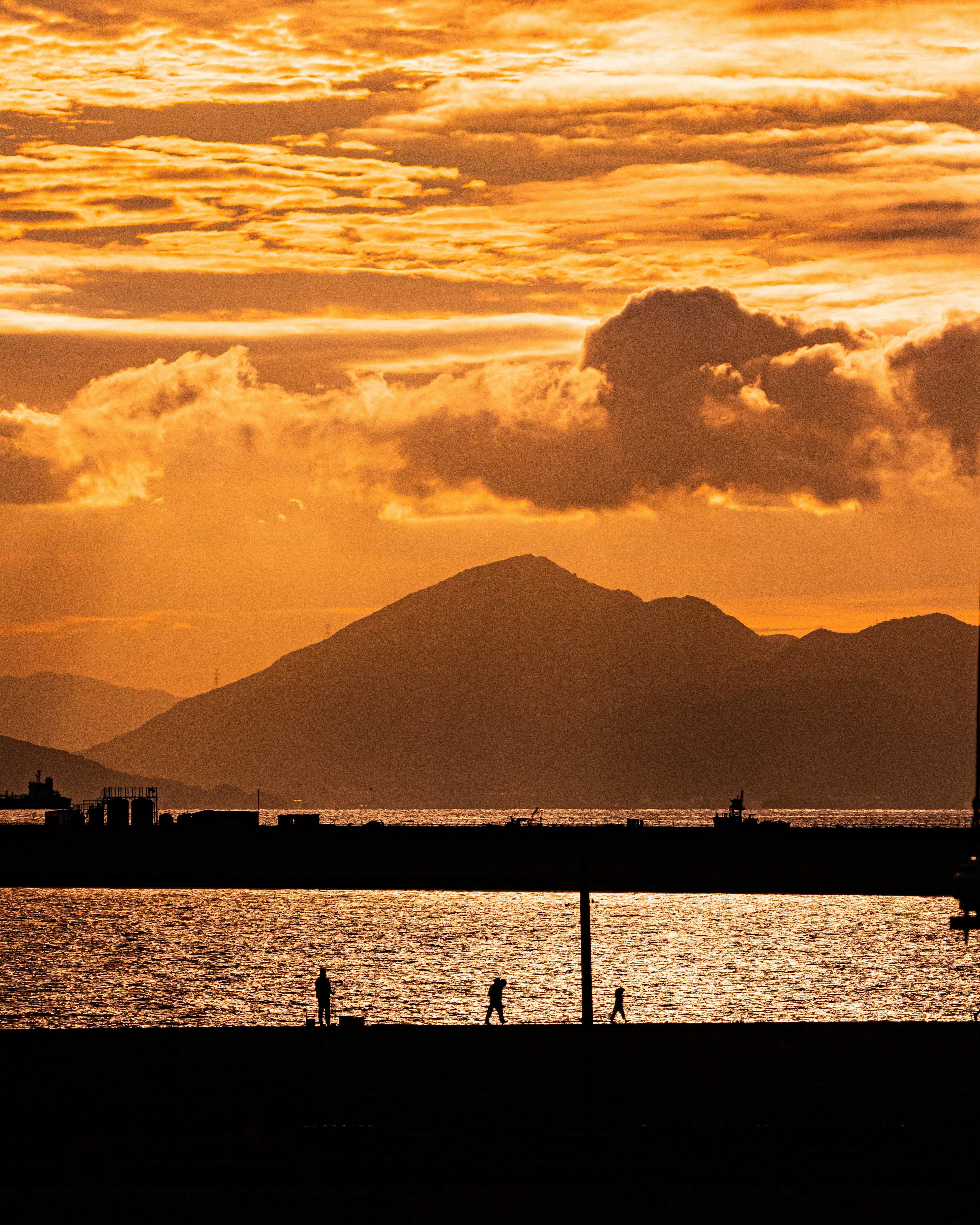 Silhouette of people walking by the sea with mountains and sunset