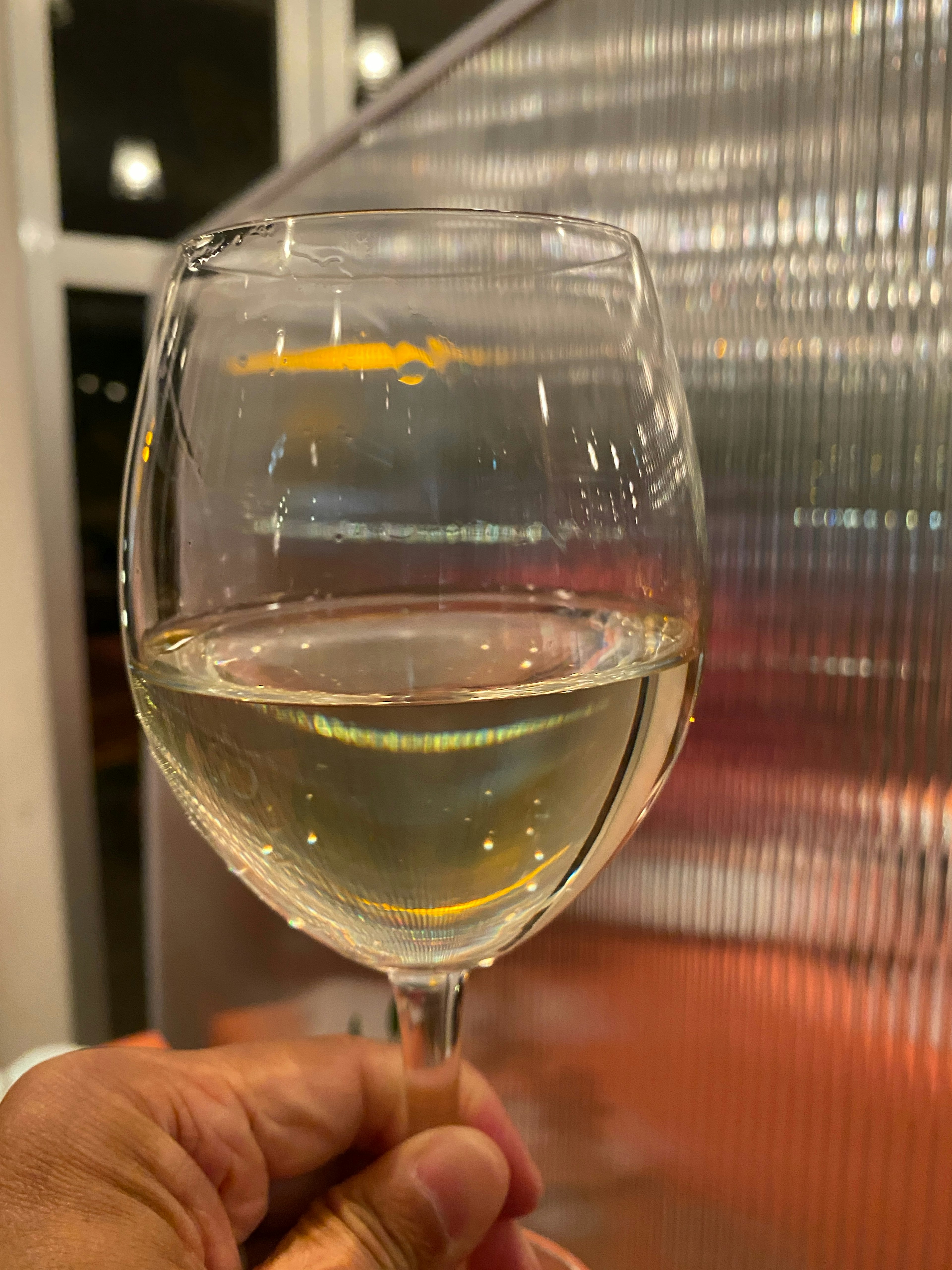 Primer plano de una mano sosteniendo una copa de vino blanco con un fondo metálico