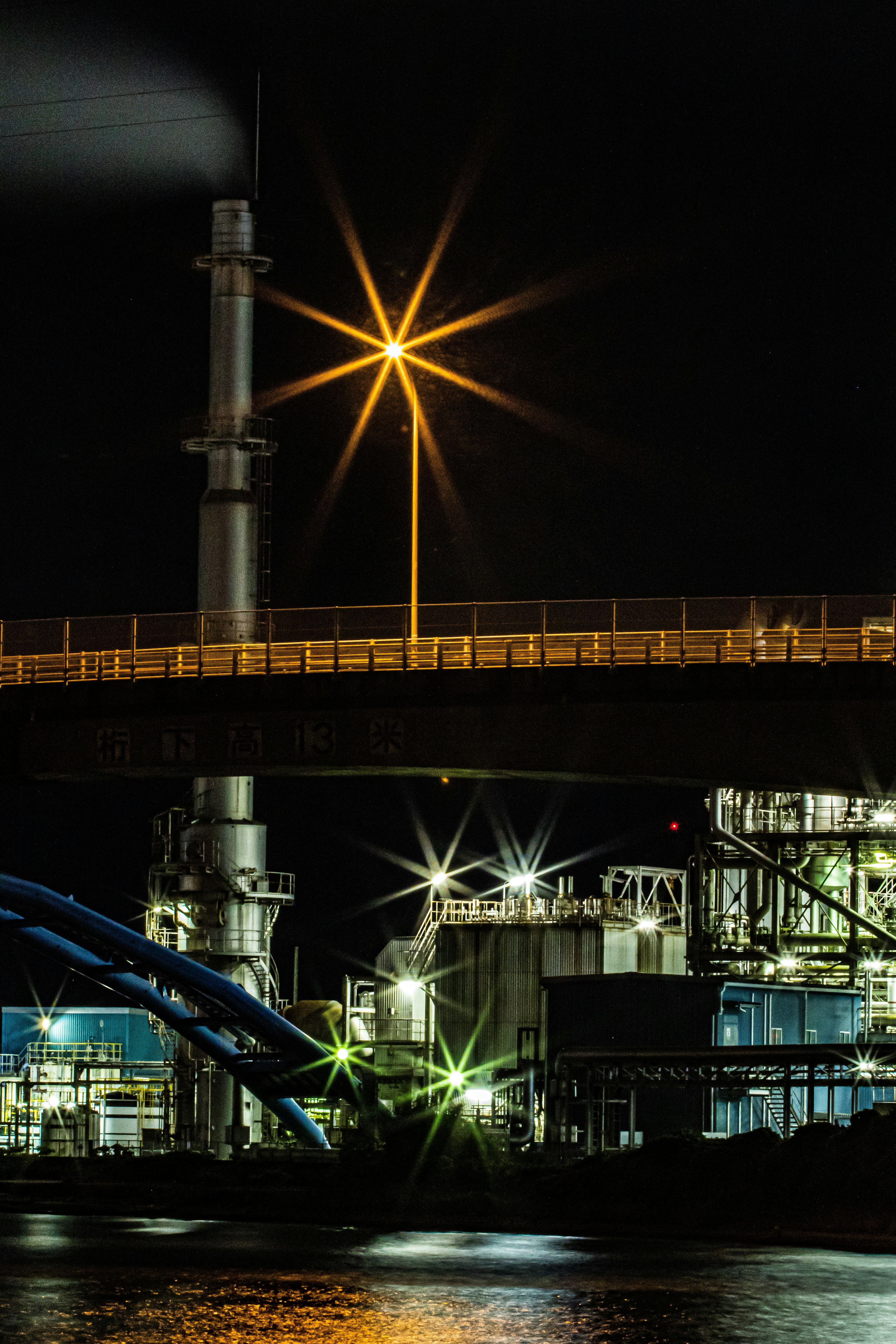 Scena industriale notturna con lampione del ponte illuminato e camino attrezzature di fabbrica riflesse sull'acqua