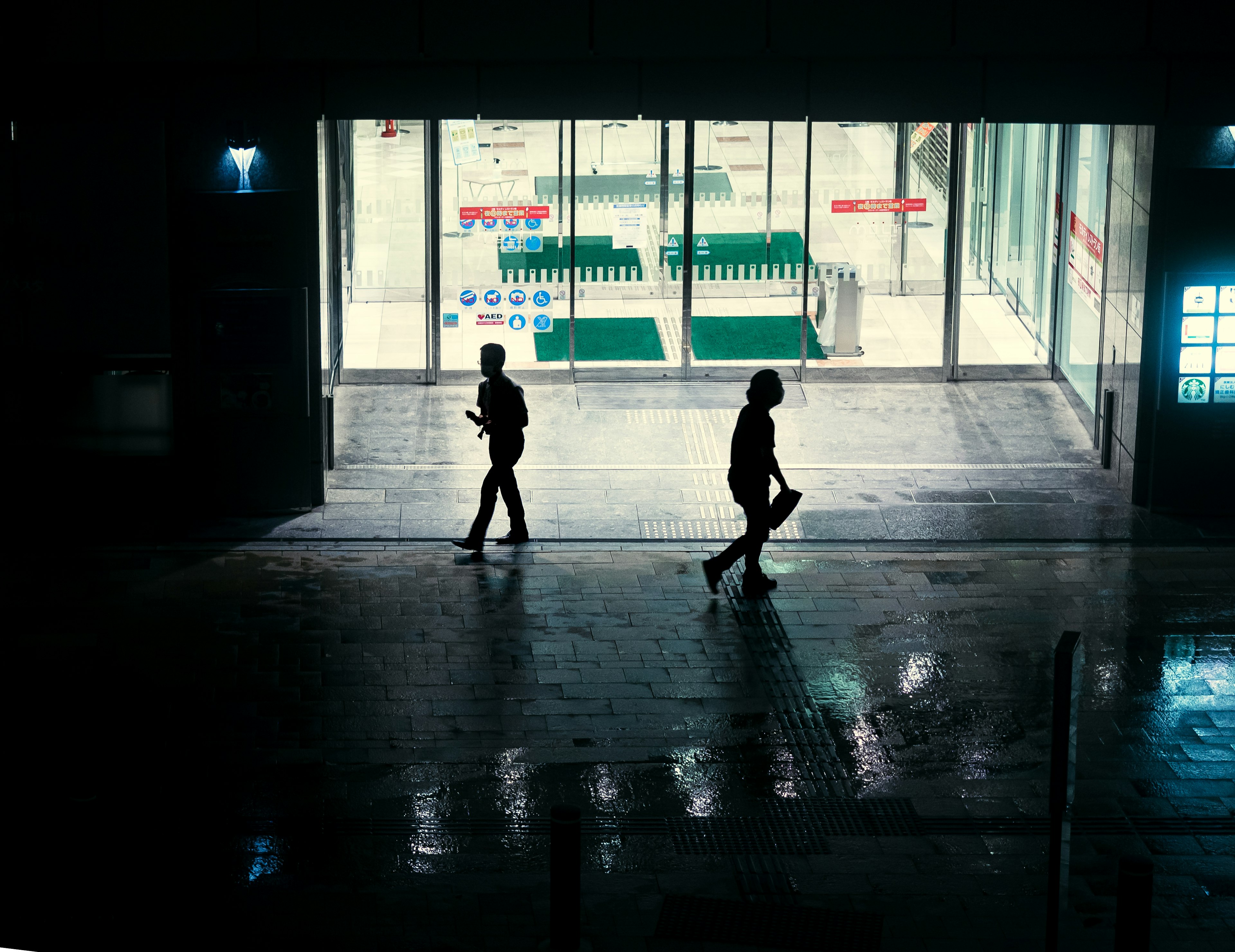 Silhouettes de deux personnes marchant dans un couloir sombre avec un fond lumineux