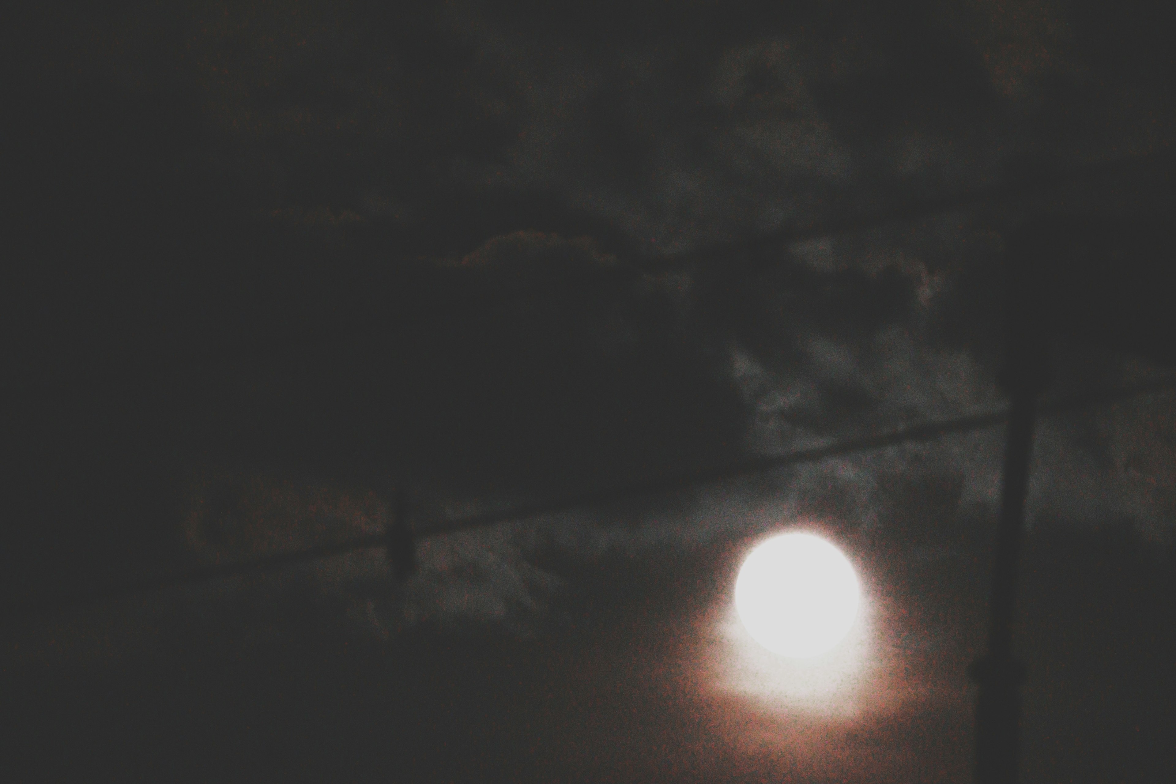 Night scene with a glowing moon partially obscured by clouds