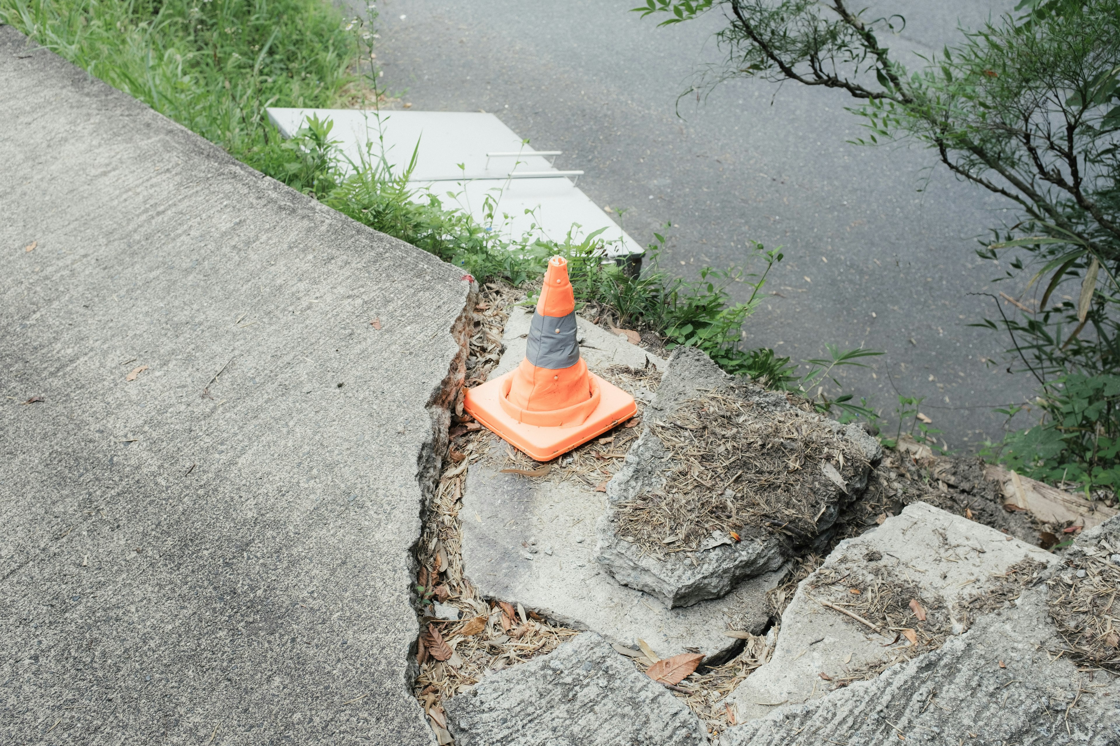 Orange traffic cone placed on cracked concrete at the edge of a road