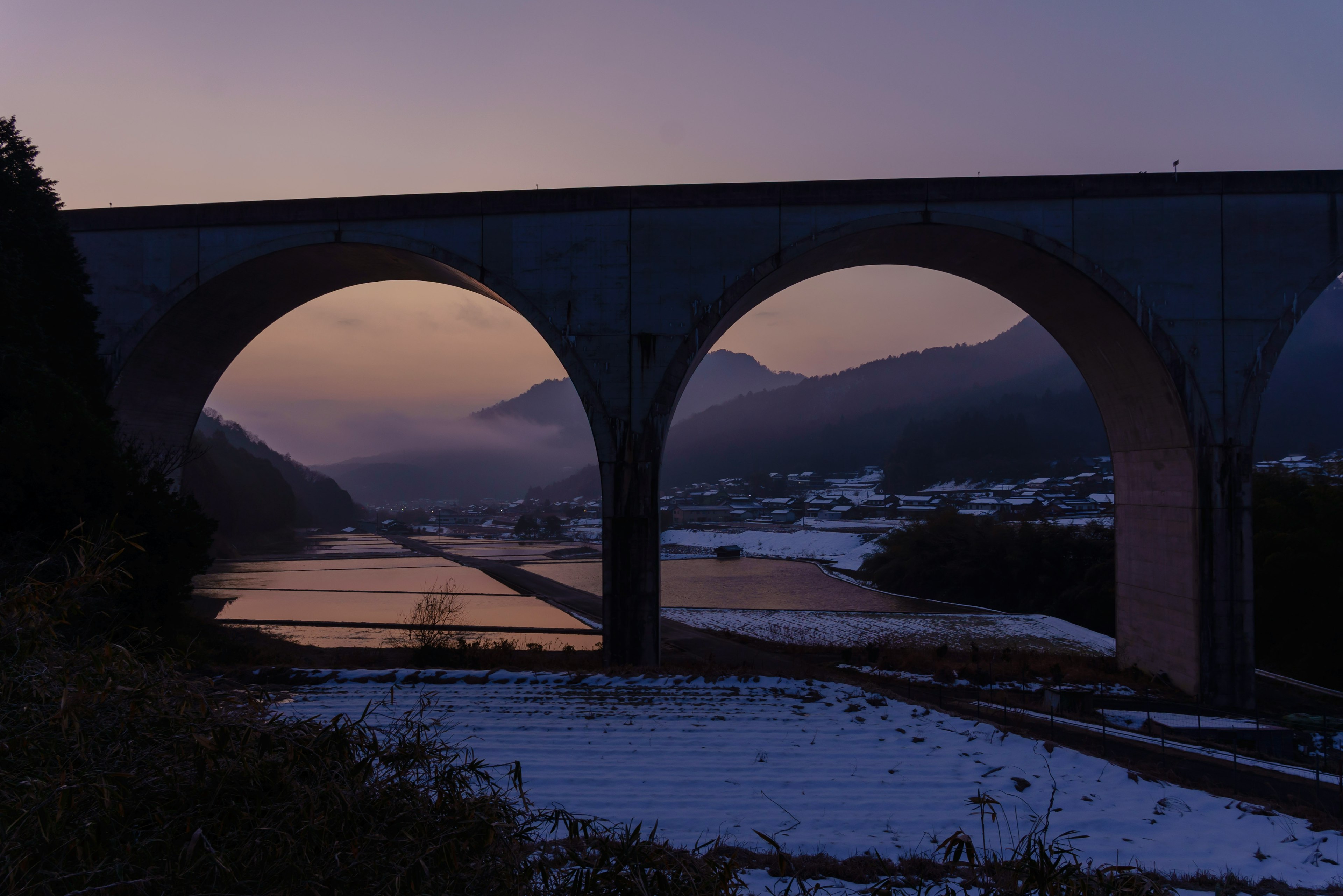 Ponte ad arco in un paesaggio innevato con montagne al crepuscolo