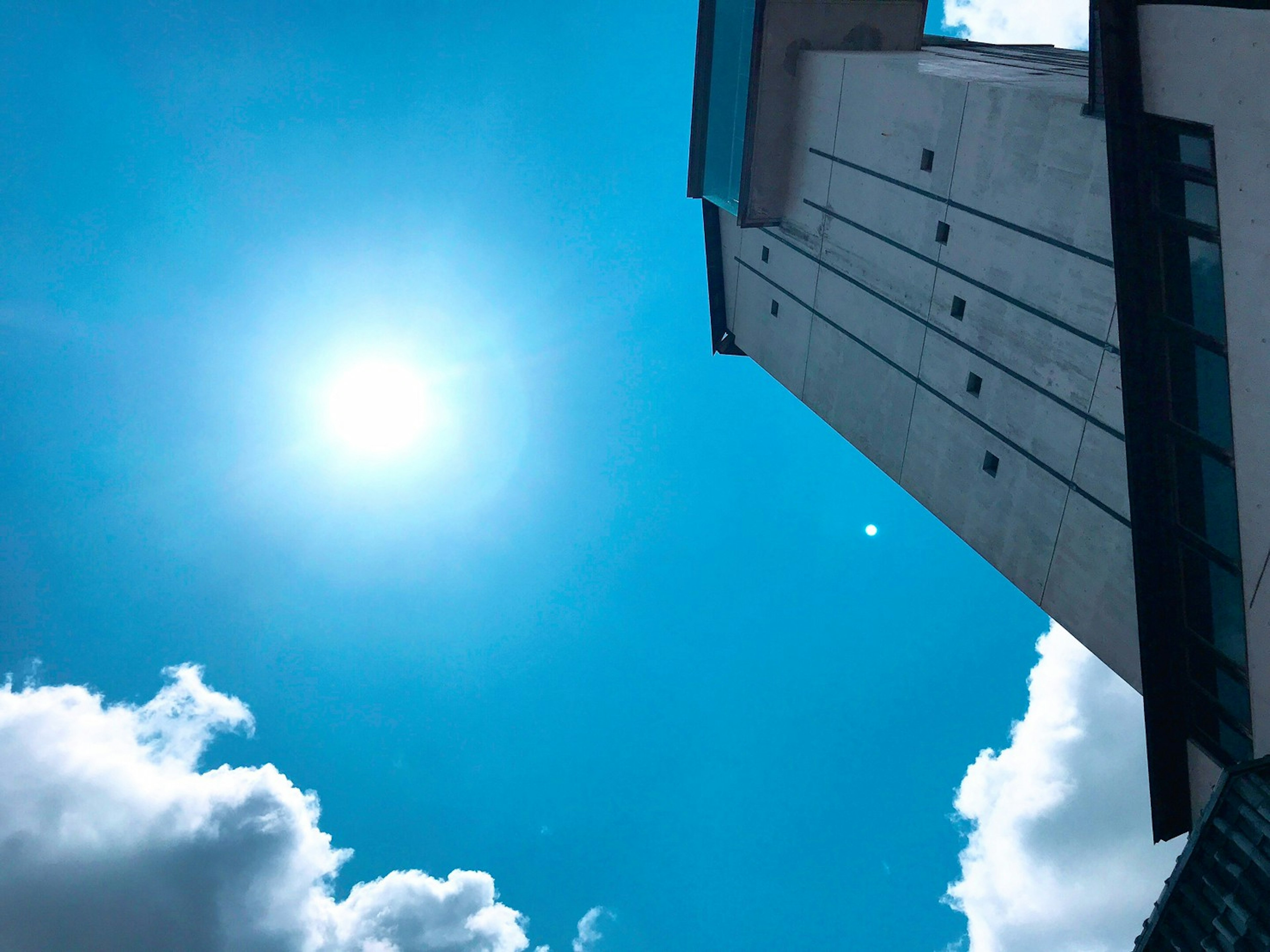 Foto eines hohen Gebäudes vor einem hellblauen Himmel mit Wolken