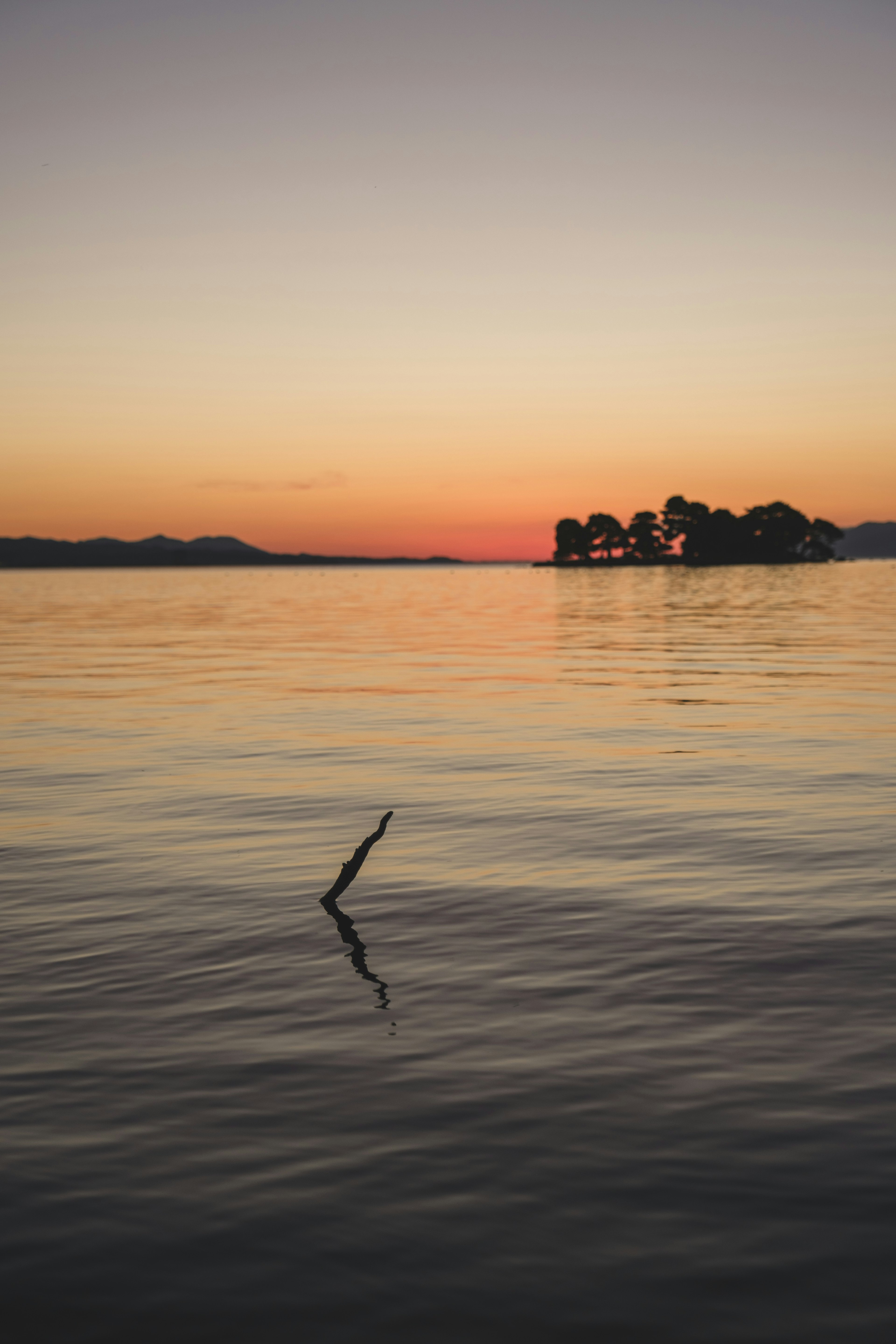 Calm lake water reflecting sunset and a small island