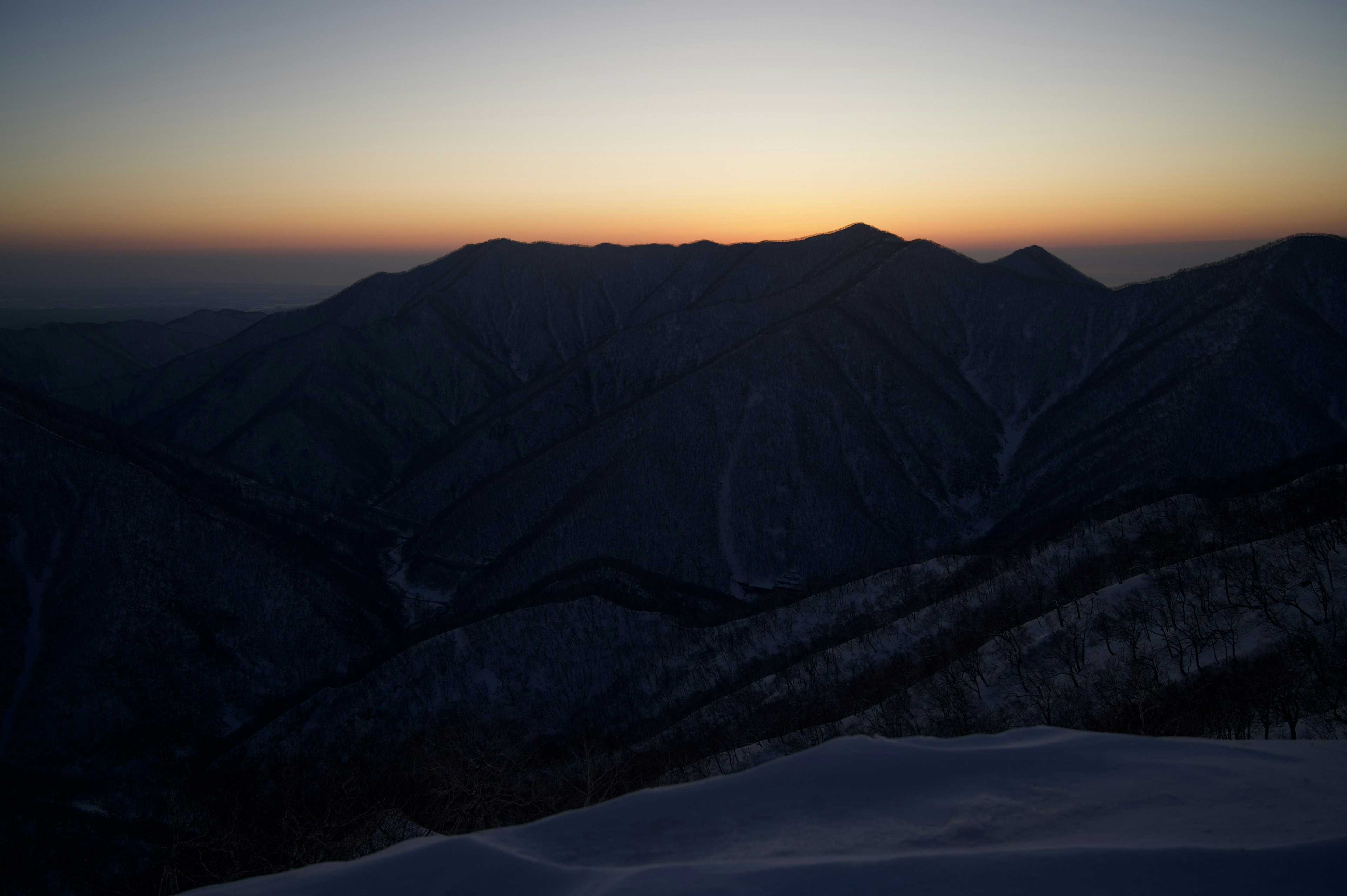 Silhouette of mountains at dusk with snowy slopes