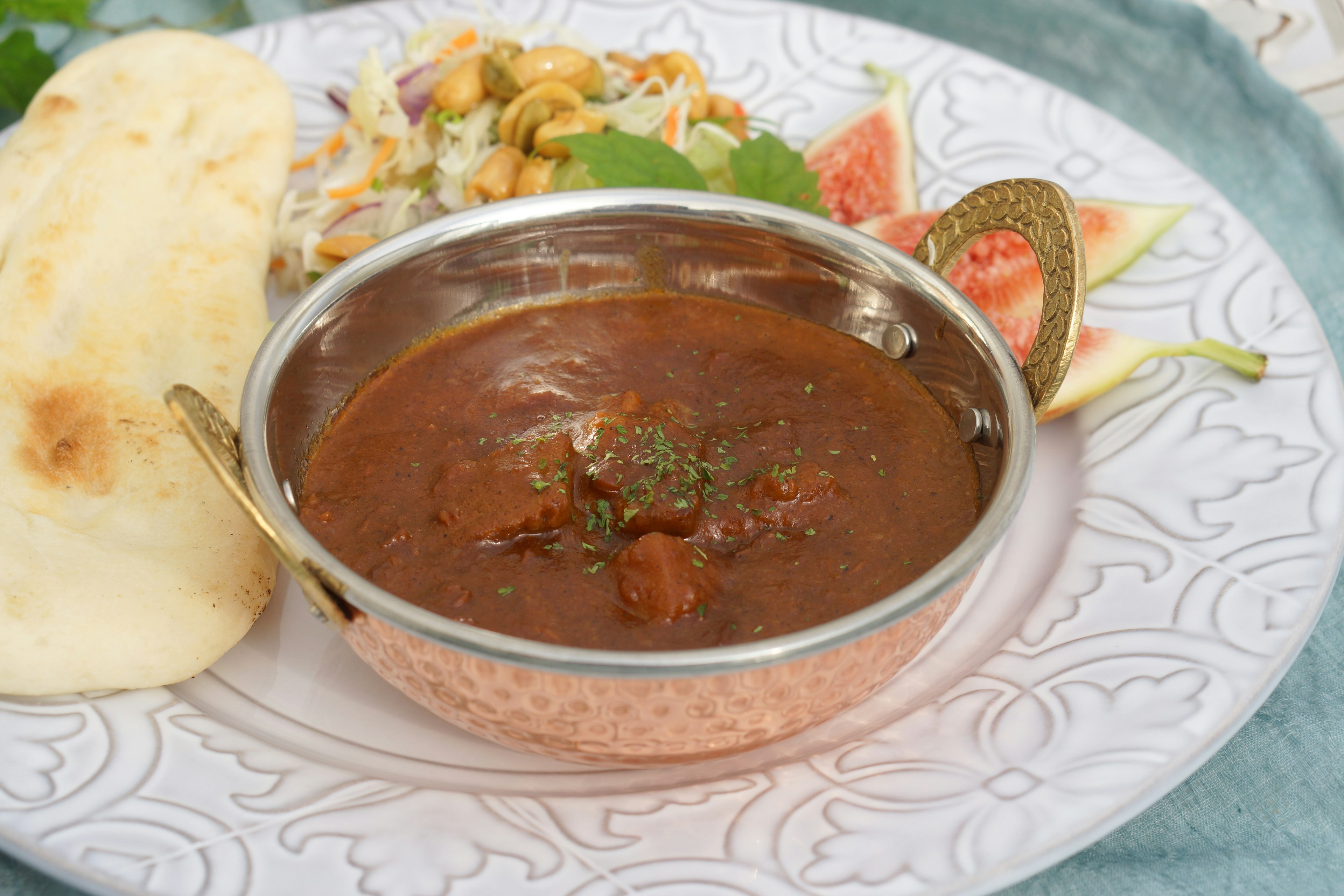 Ein Gericht mit scharfem Curry und Naan, begleitet von frischem Salat und Obst