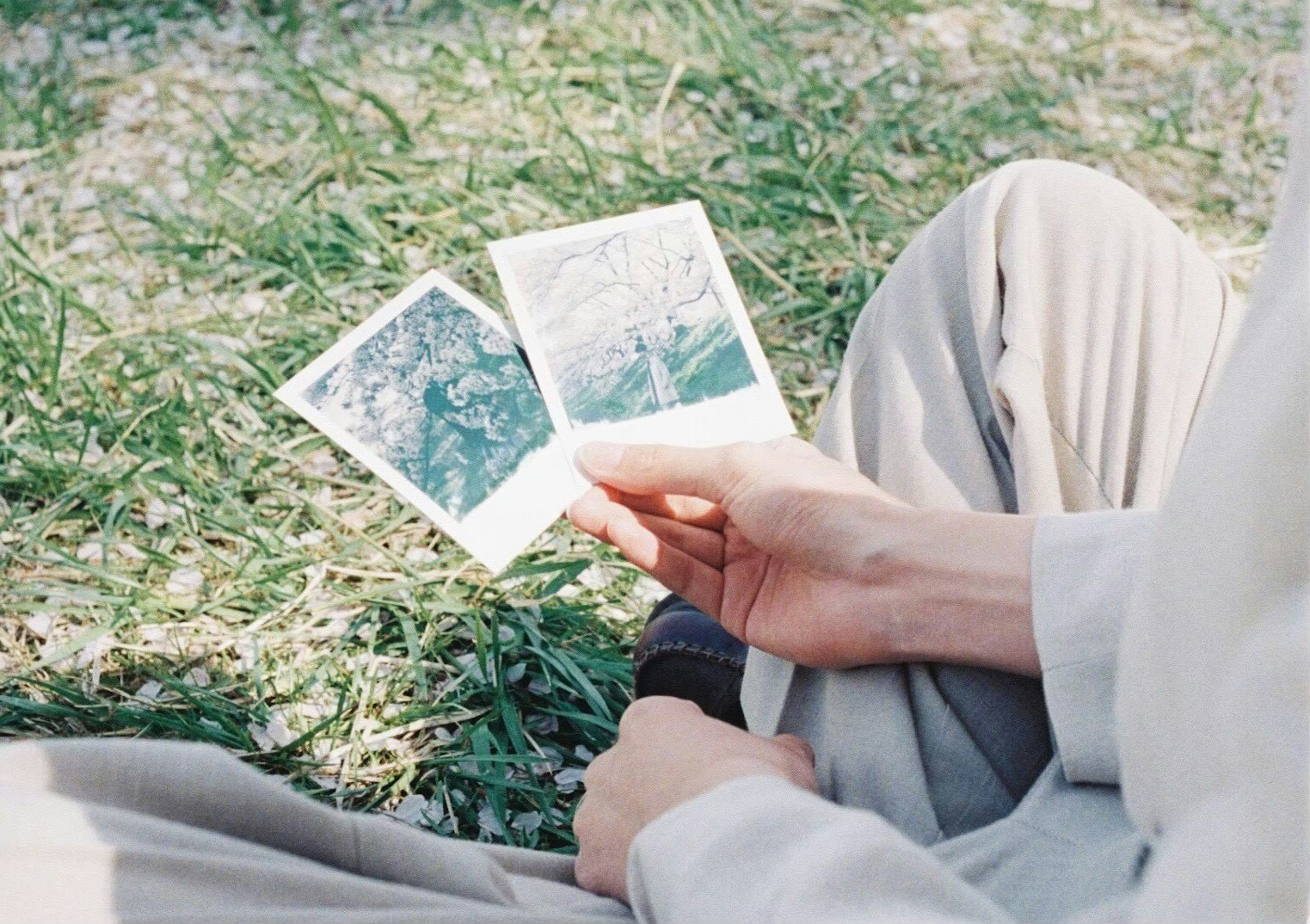 Une personne assise sur l'herbe tenant deux photographies