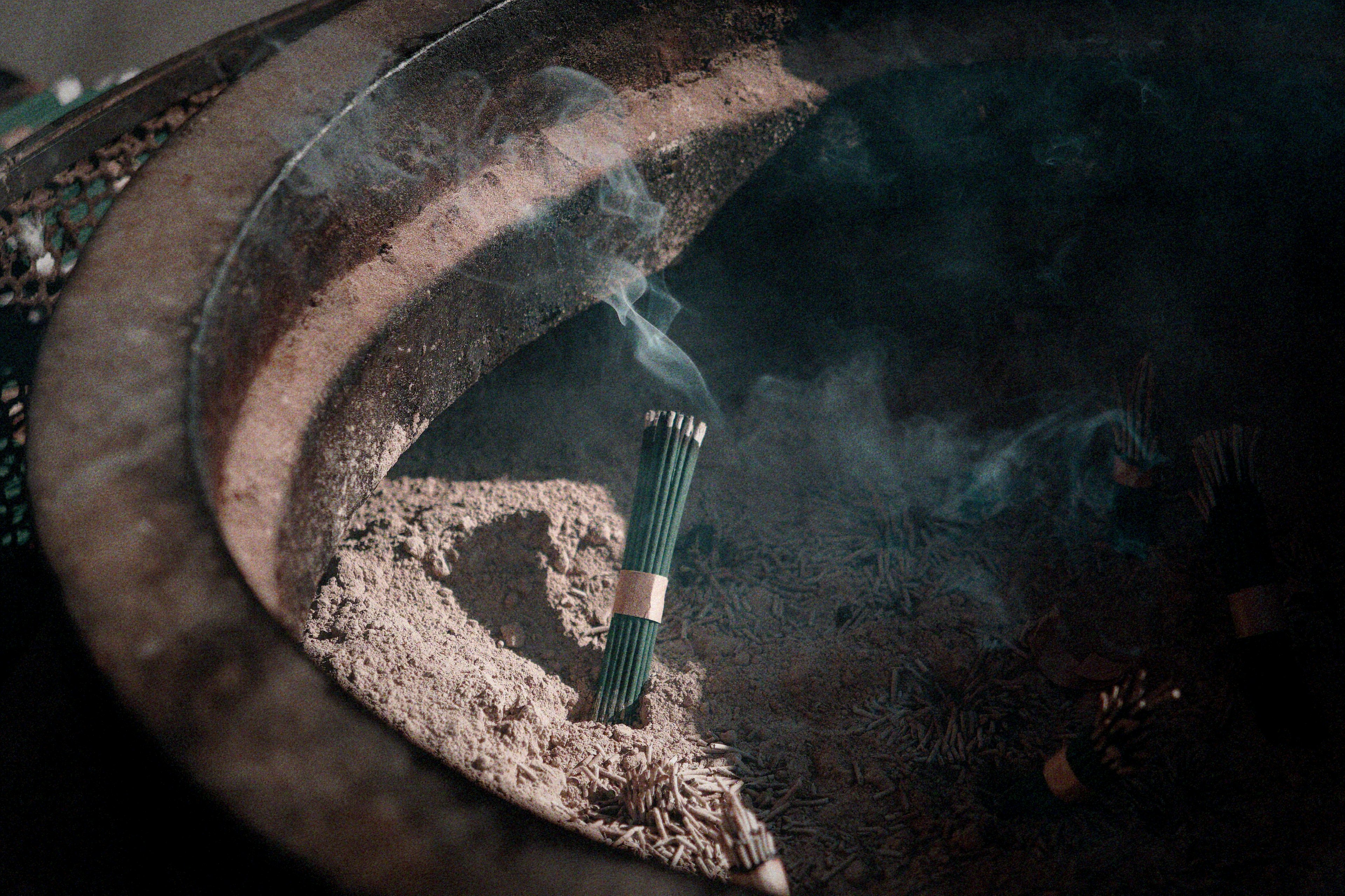 Incense stick burning in a traditional incense burner surrounded by ash and smoke