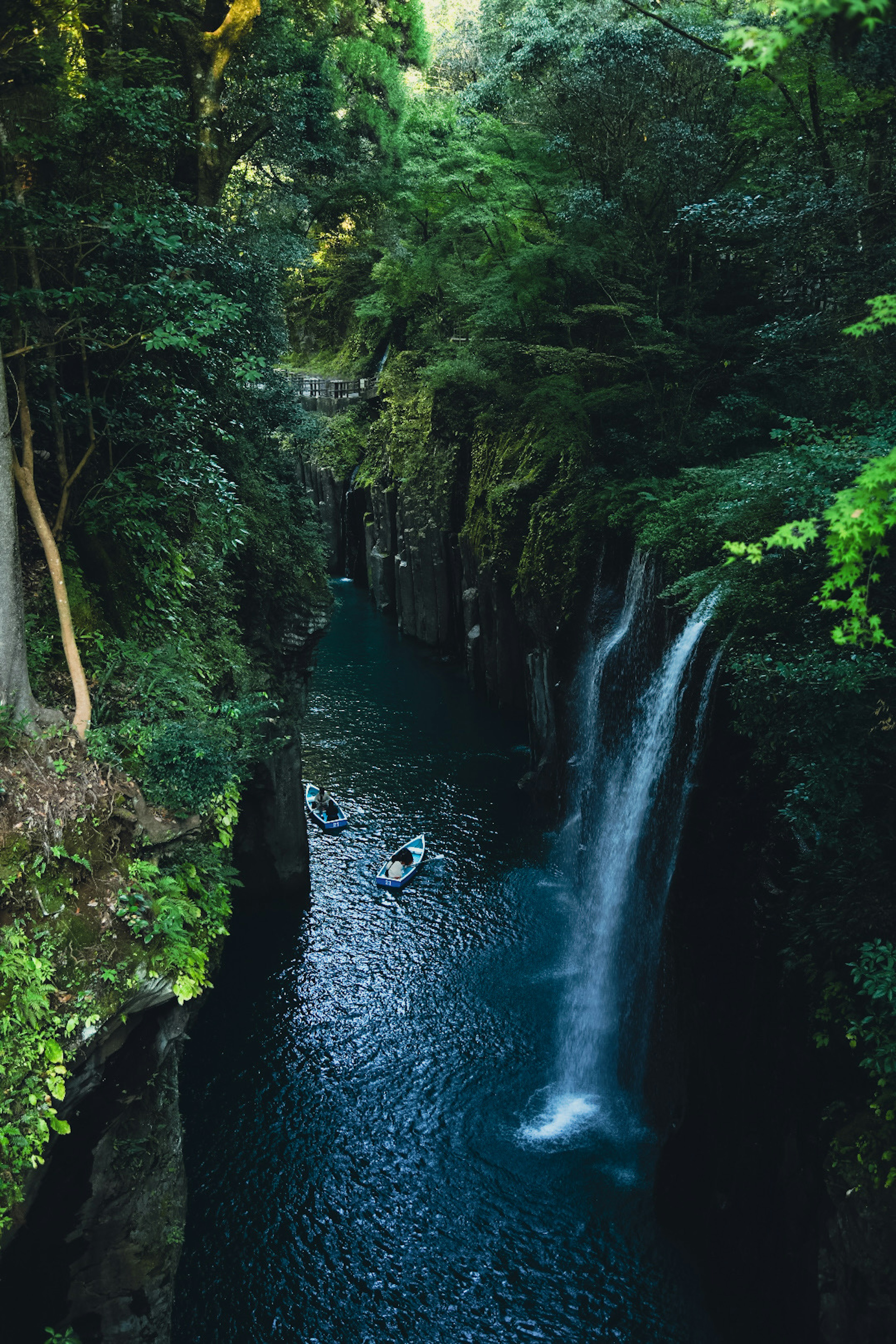 Malersiche Aussicht auf einen Wasserfall in einer üppigen Schlucht mit kleinen Booten auf dem ruhigen Wasser