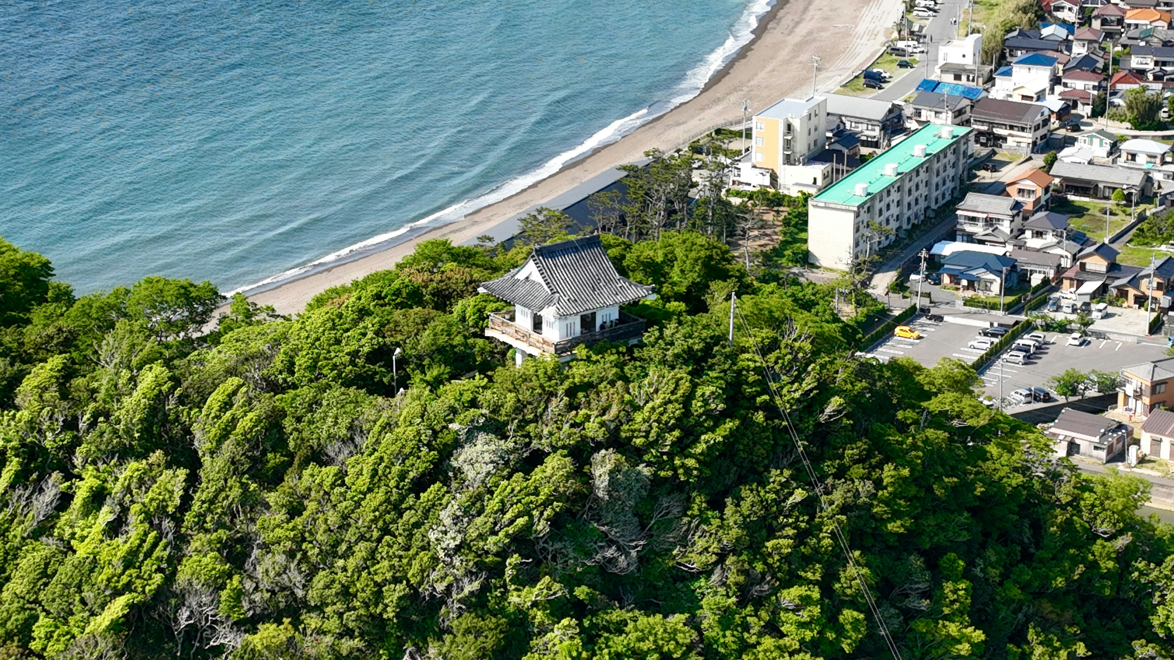 Scenic view of a temple on a lush hill near the coast with a beach and town