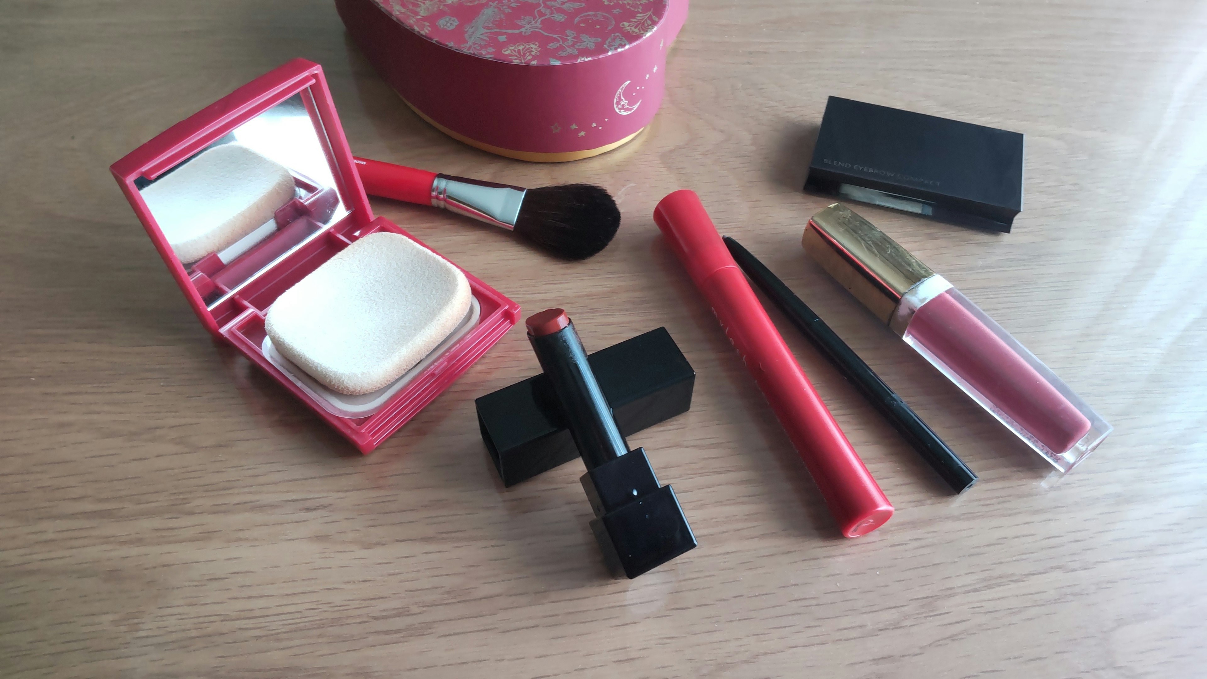 A set of cosmetics including red lipstick, eyeliner, brush, and powder case