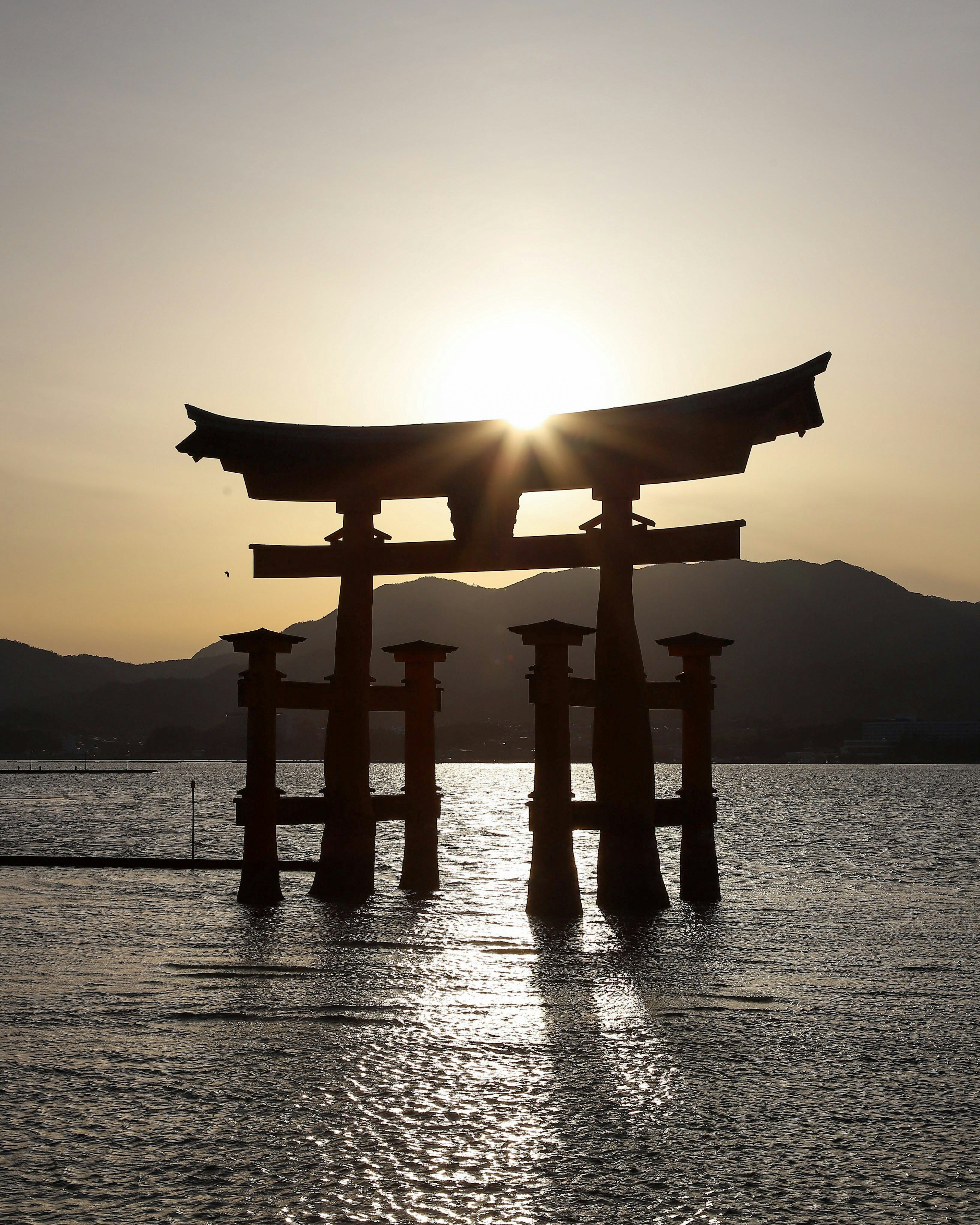 Torii gate silhouetted against a sunset over water