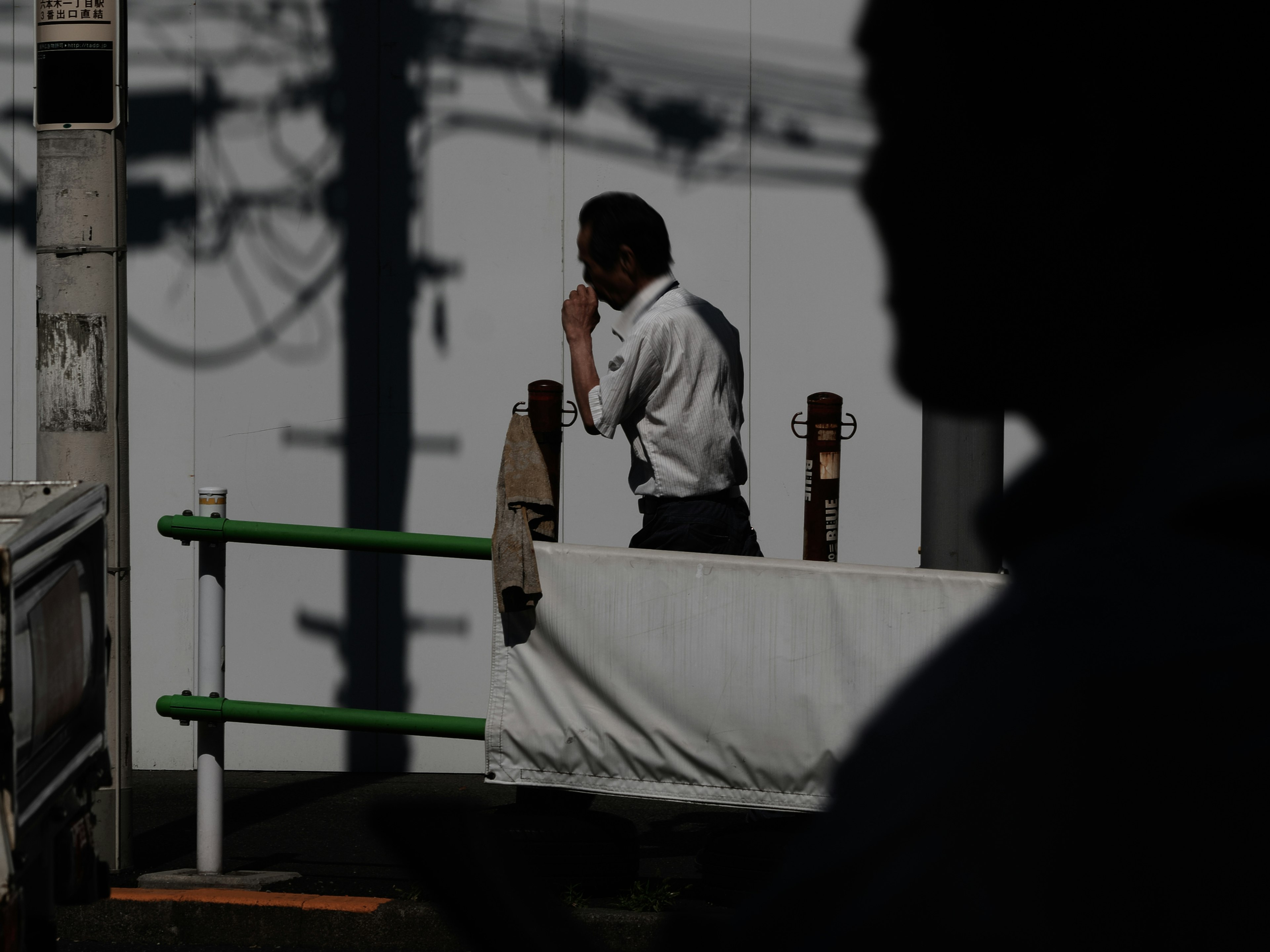 A silhouette of a man smoking while walking with power lines in the background