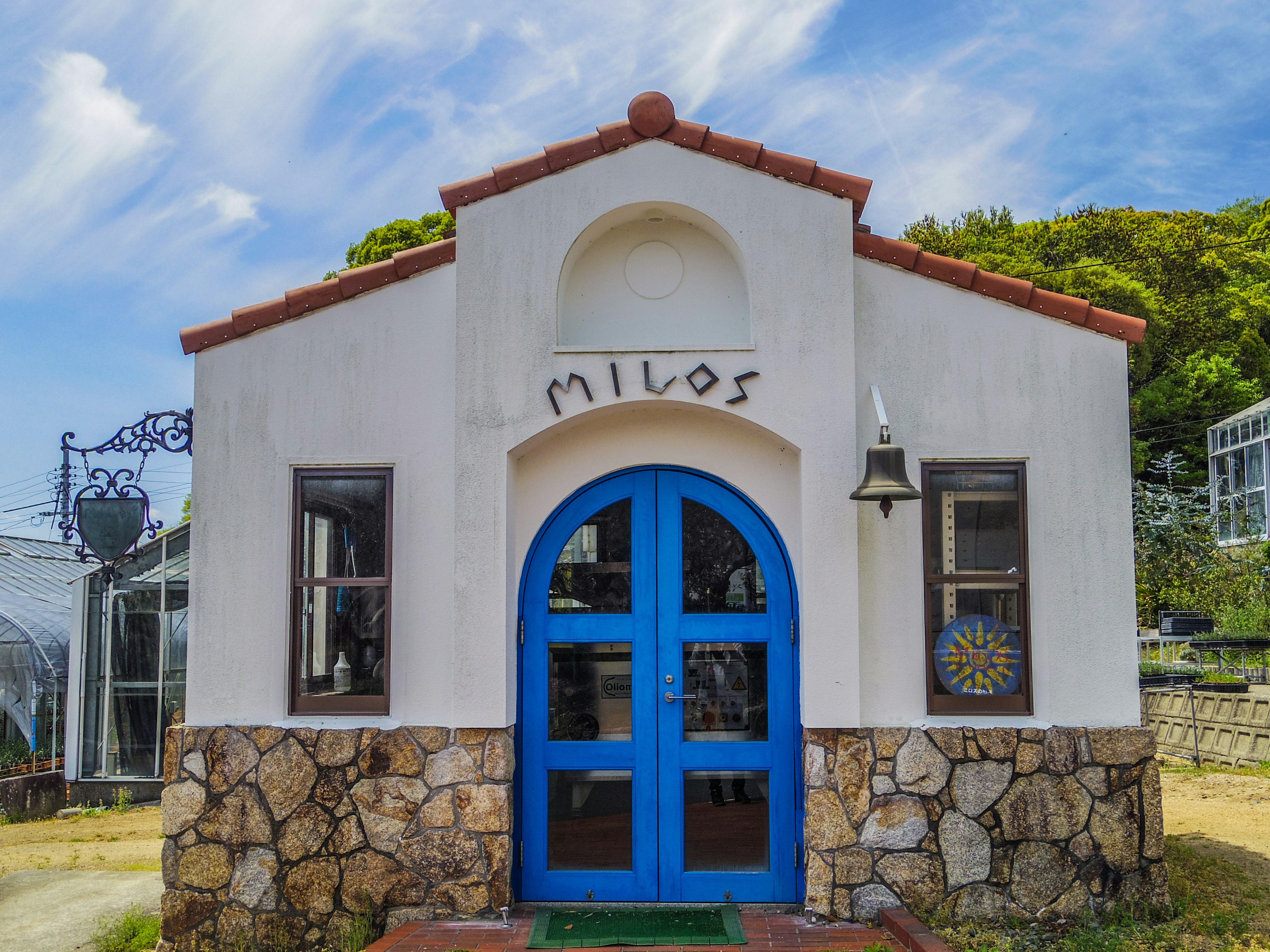 Exterior de un edificio blanco con una puerta y techo azules que lleva el nombre Milos