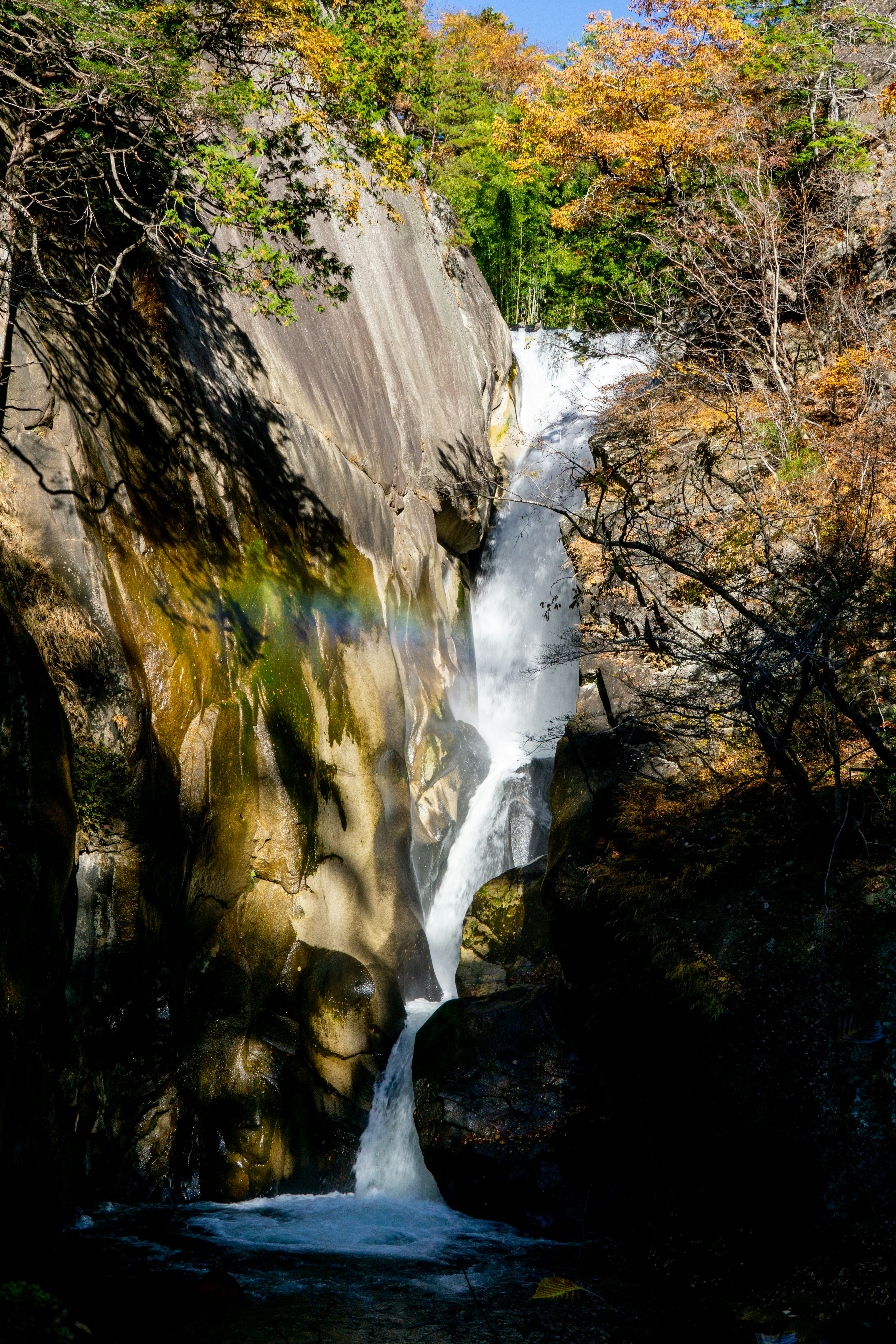 Air terjun yang indah mengalir di atas batu dikelilingi oleh dedaunan musim gugur