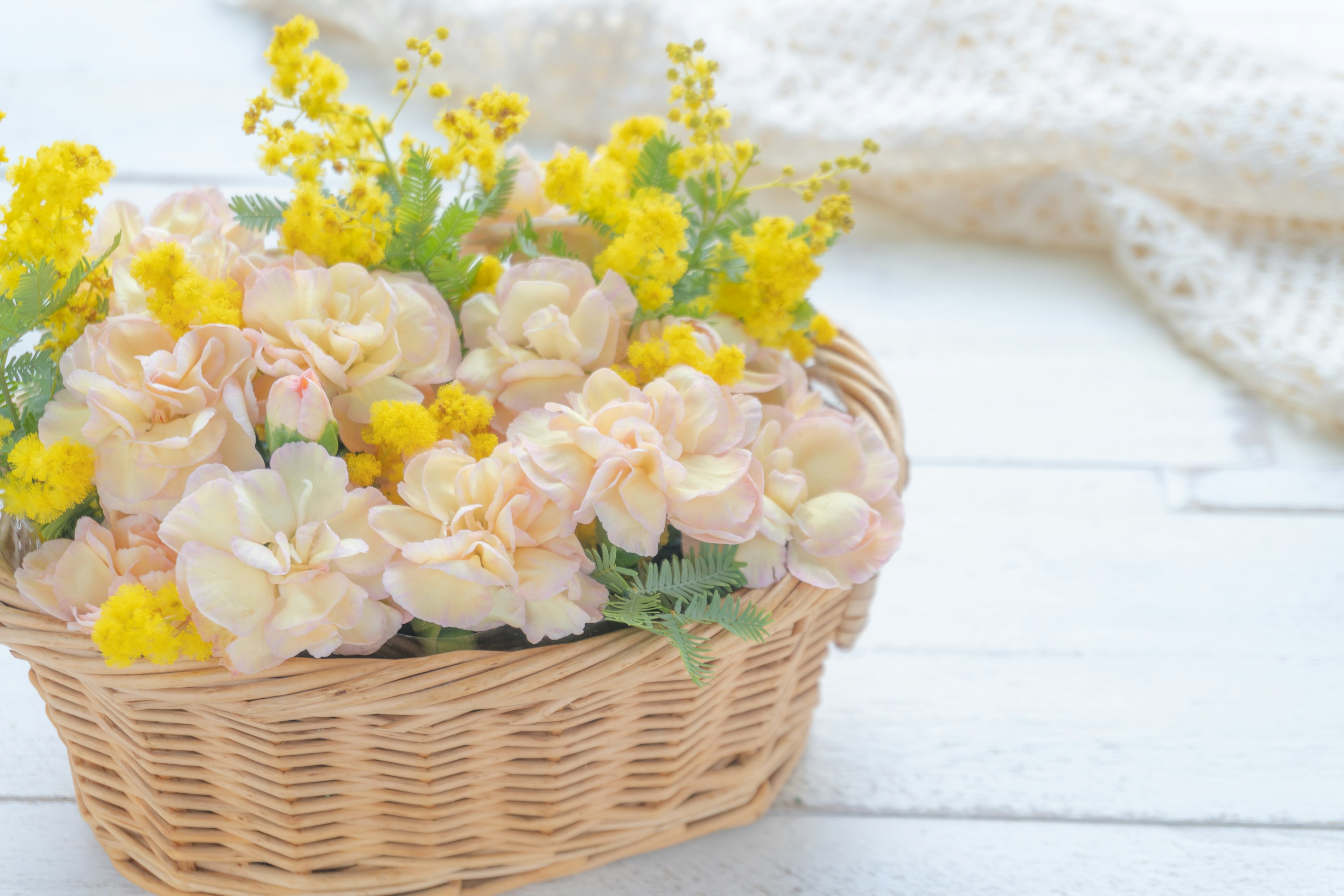 Una cesta de mimbre llena de flores suaves en tonos rosa y amarillo con un tejido de punto blanco