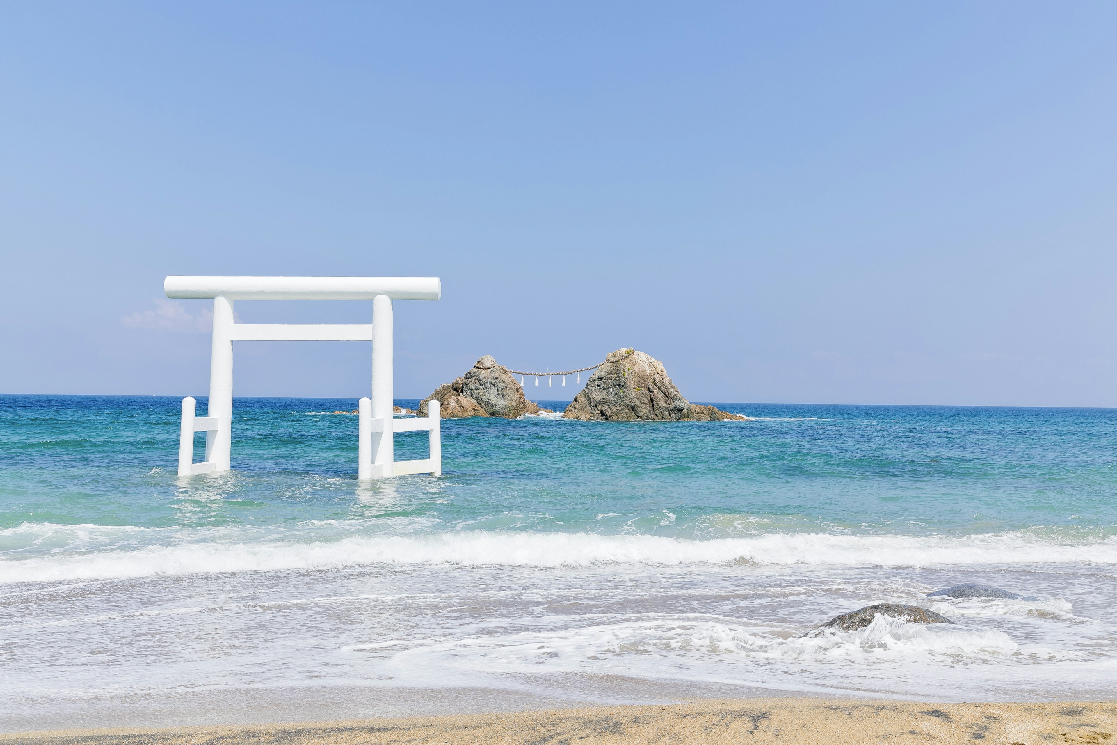 Beach scene featuring a white torii gate and blue ocean