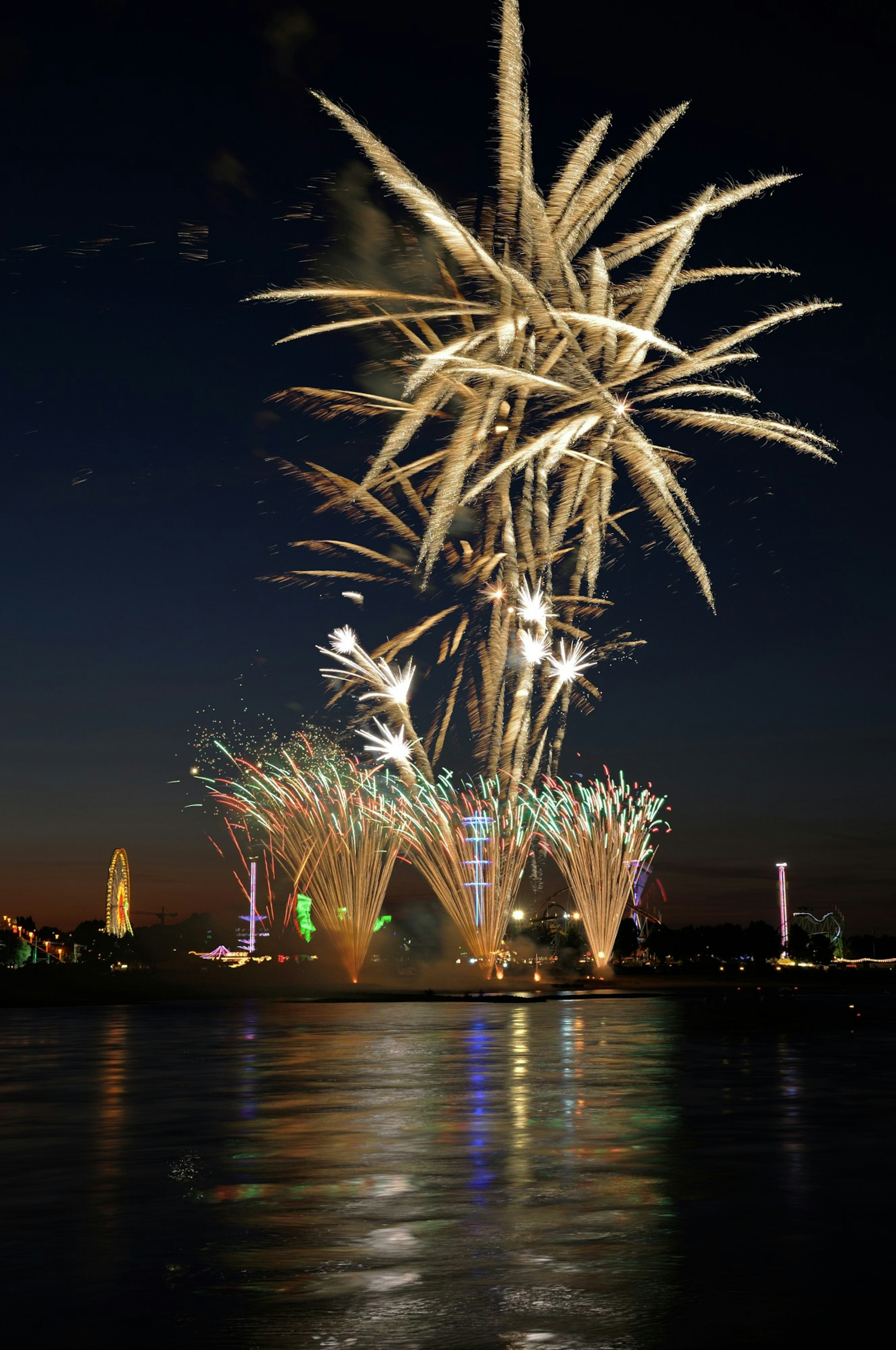 Fuegos artificiales estallando en el cielo nocturno con reflejos en el agua