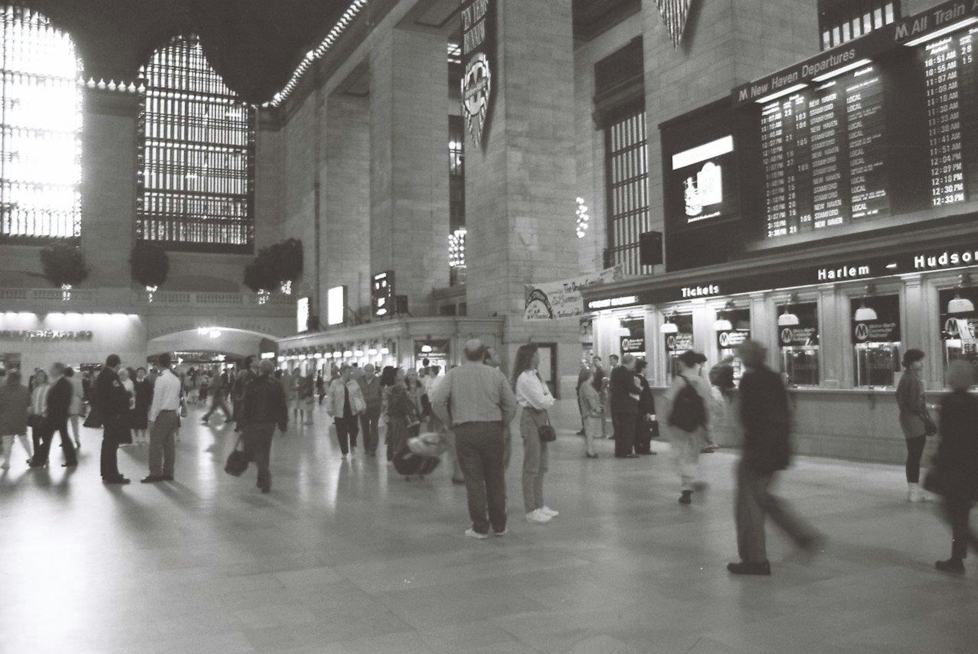 Photo en noir et blanc de l'intérieur de la gare Grand Central avec des personnes marchant et des fenêtres lumineuses