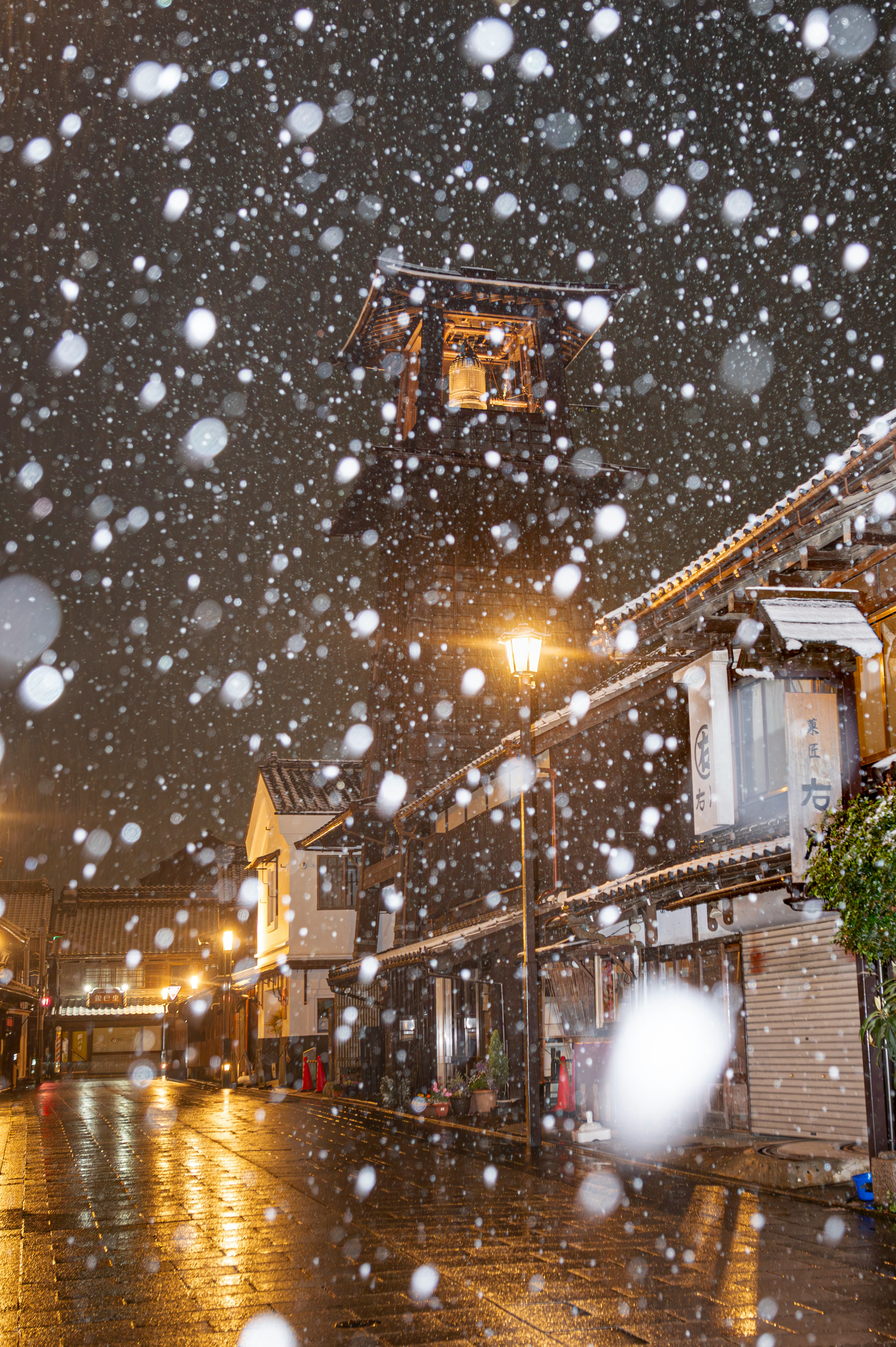 Snow falling on a street at night with a clock tower