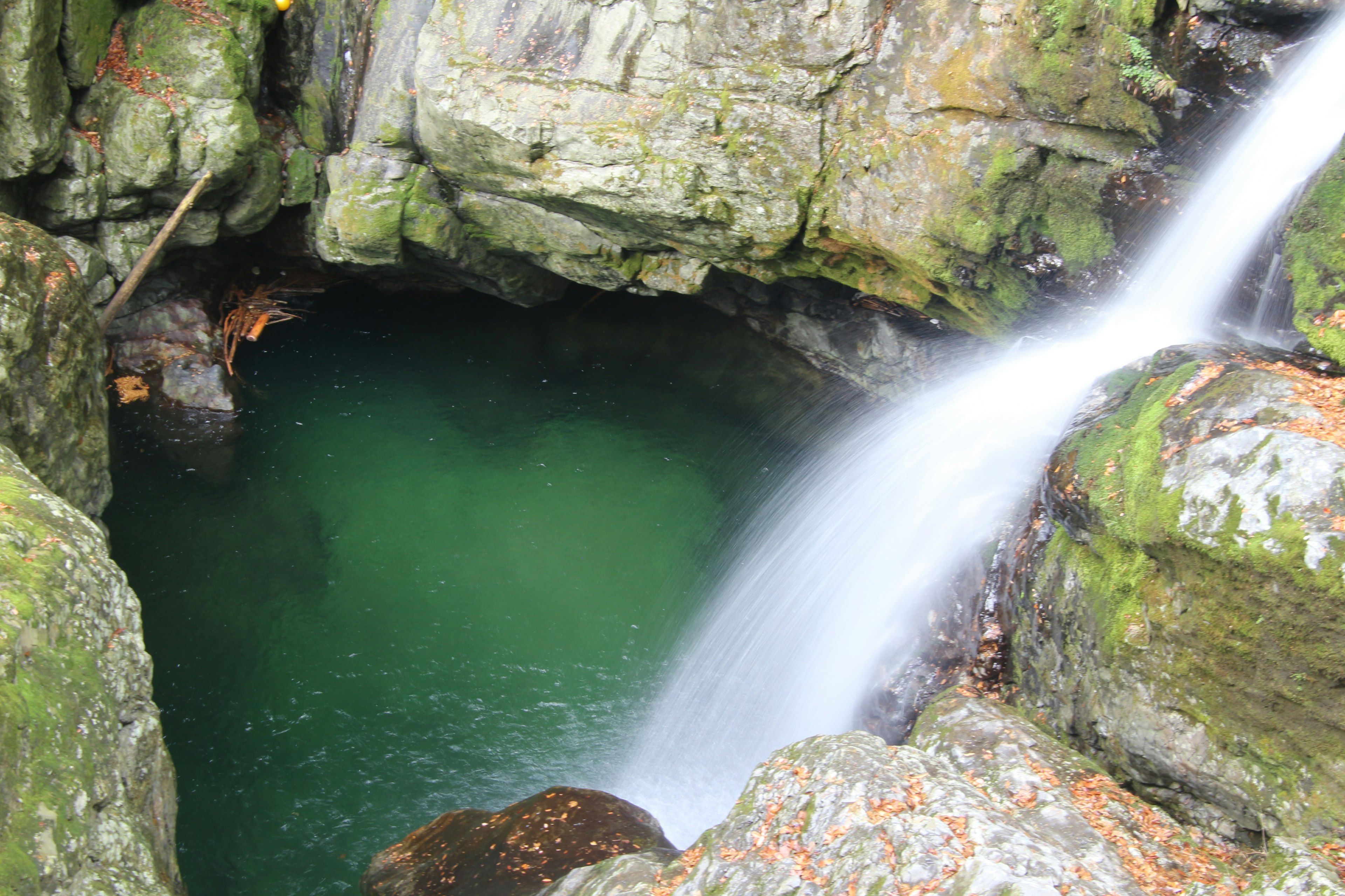 Pemandangan indah air terjun mengalir di antara batu dengan kolam air hijau yang ditutupi lumut