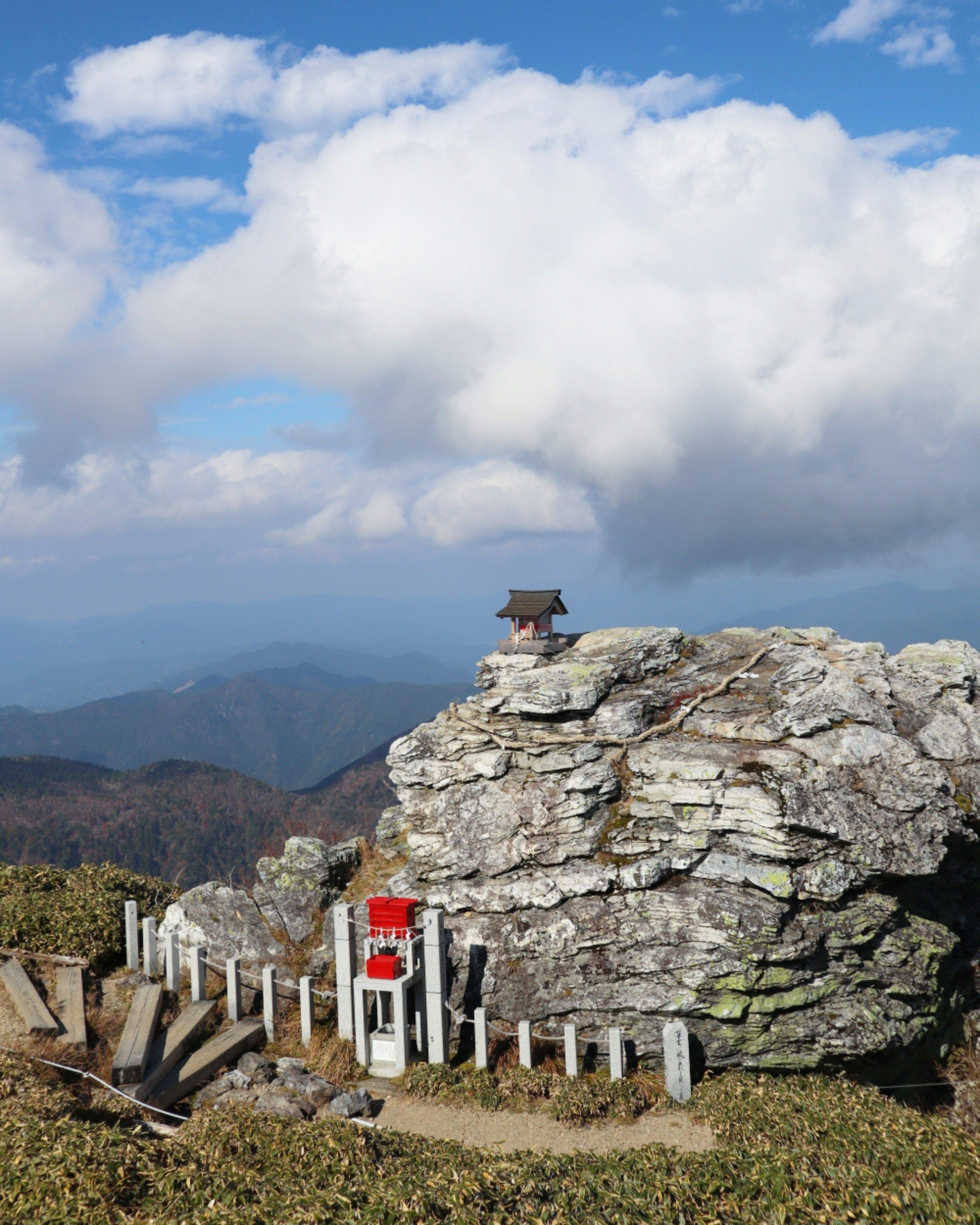 Scenic view of a large rock with a small hut on top surrounded by mountains and clouds