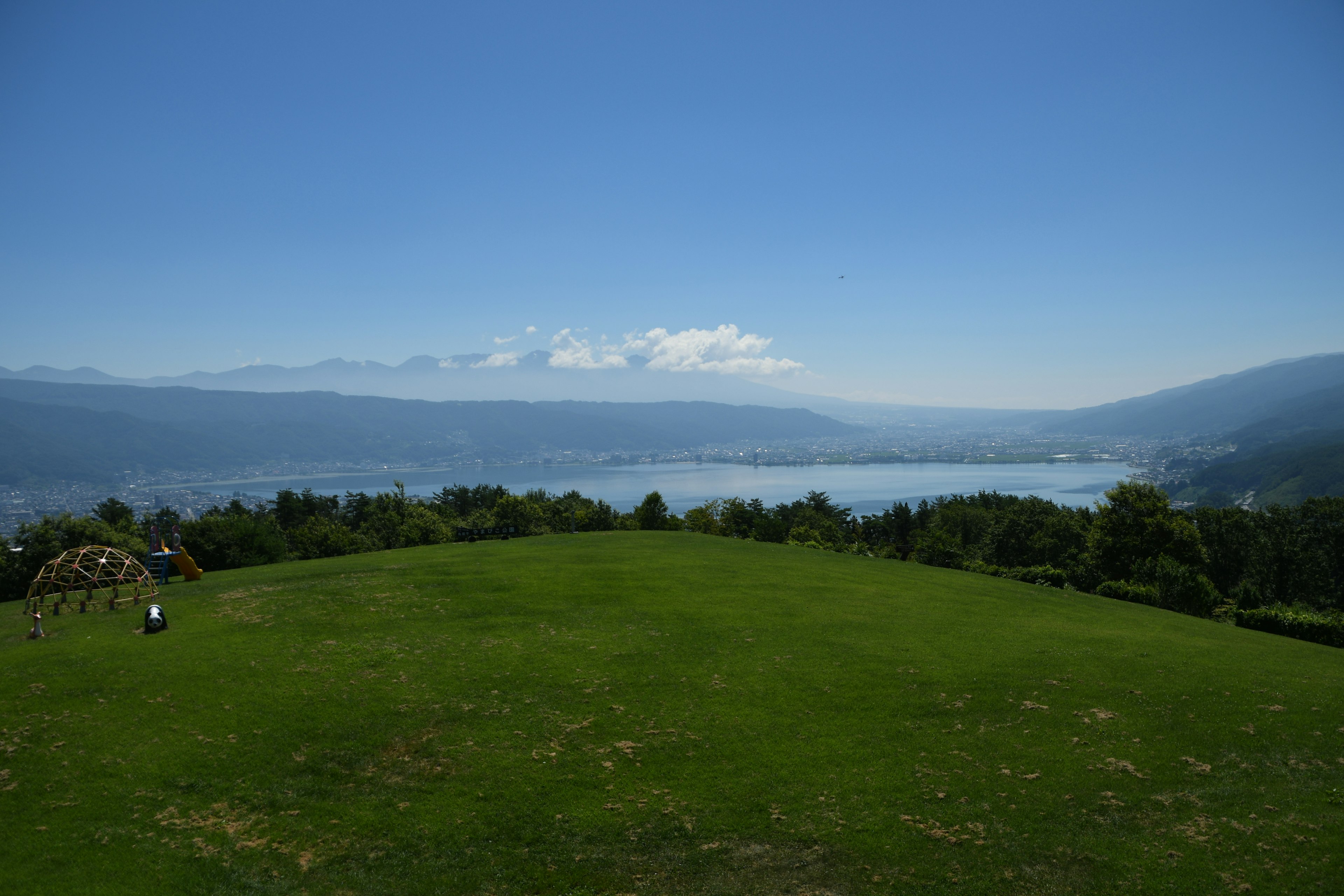 青空の下に広がる緑の草原と湖の景色