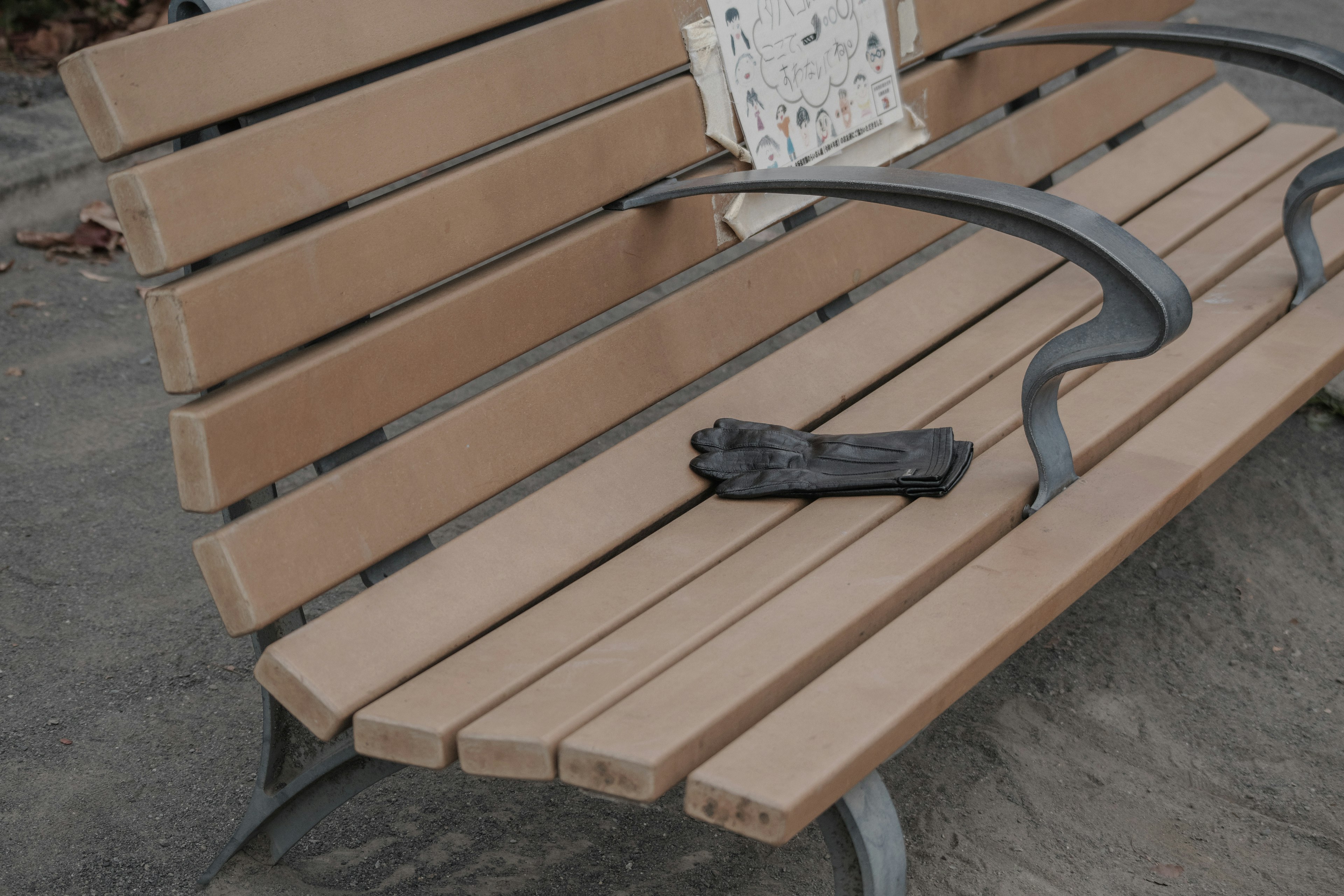 Gant noir reposant sur un banc de parc avec des lattes en bois et des bras en métal