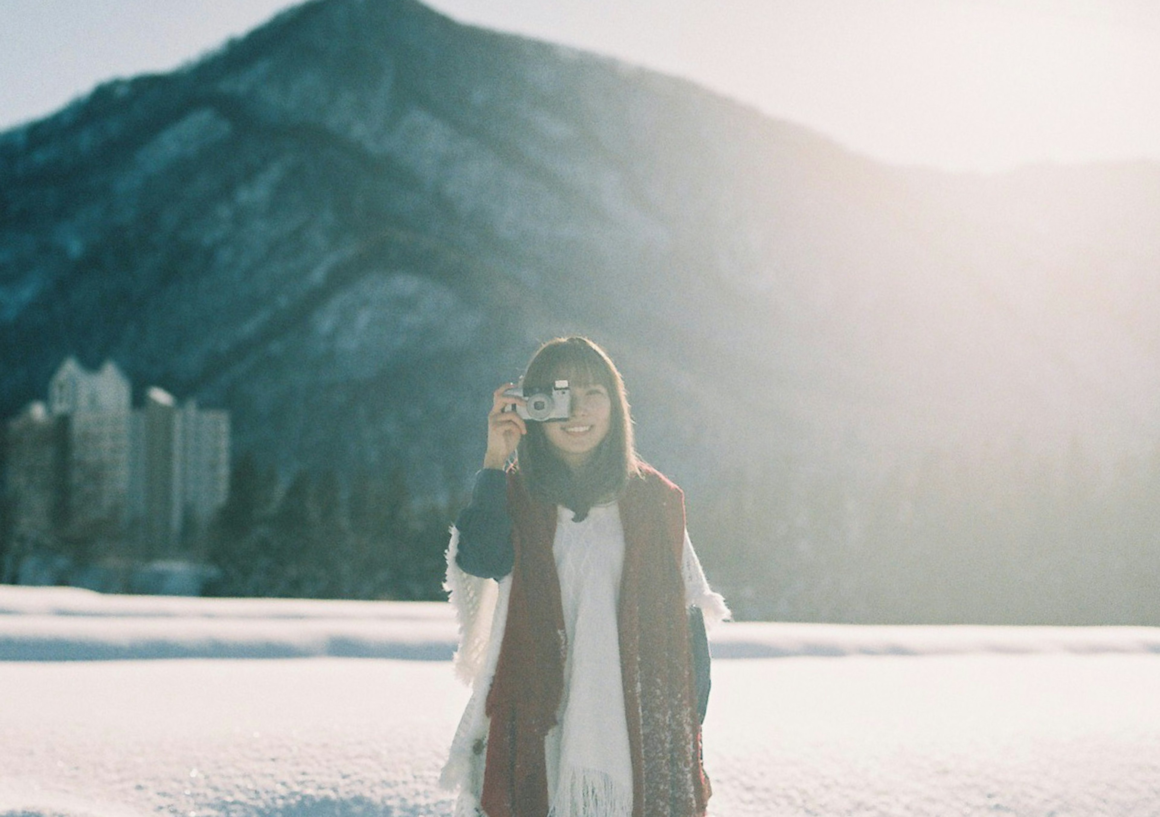 女性在雪地中拿著相機，背景是山脈