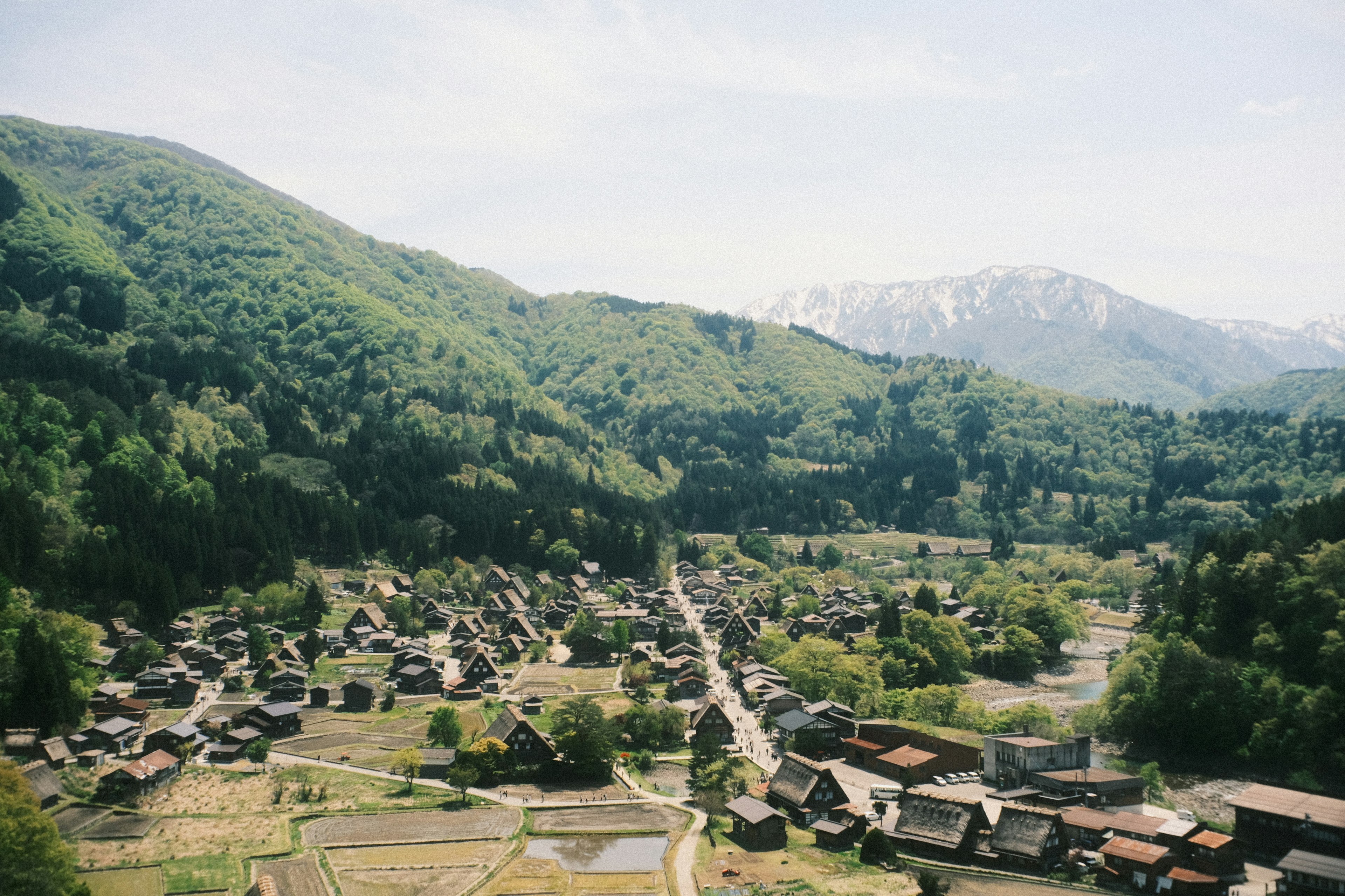 Scenic view of a village surrounded by mountains Green hills and snow-capped peaks in the background