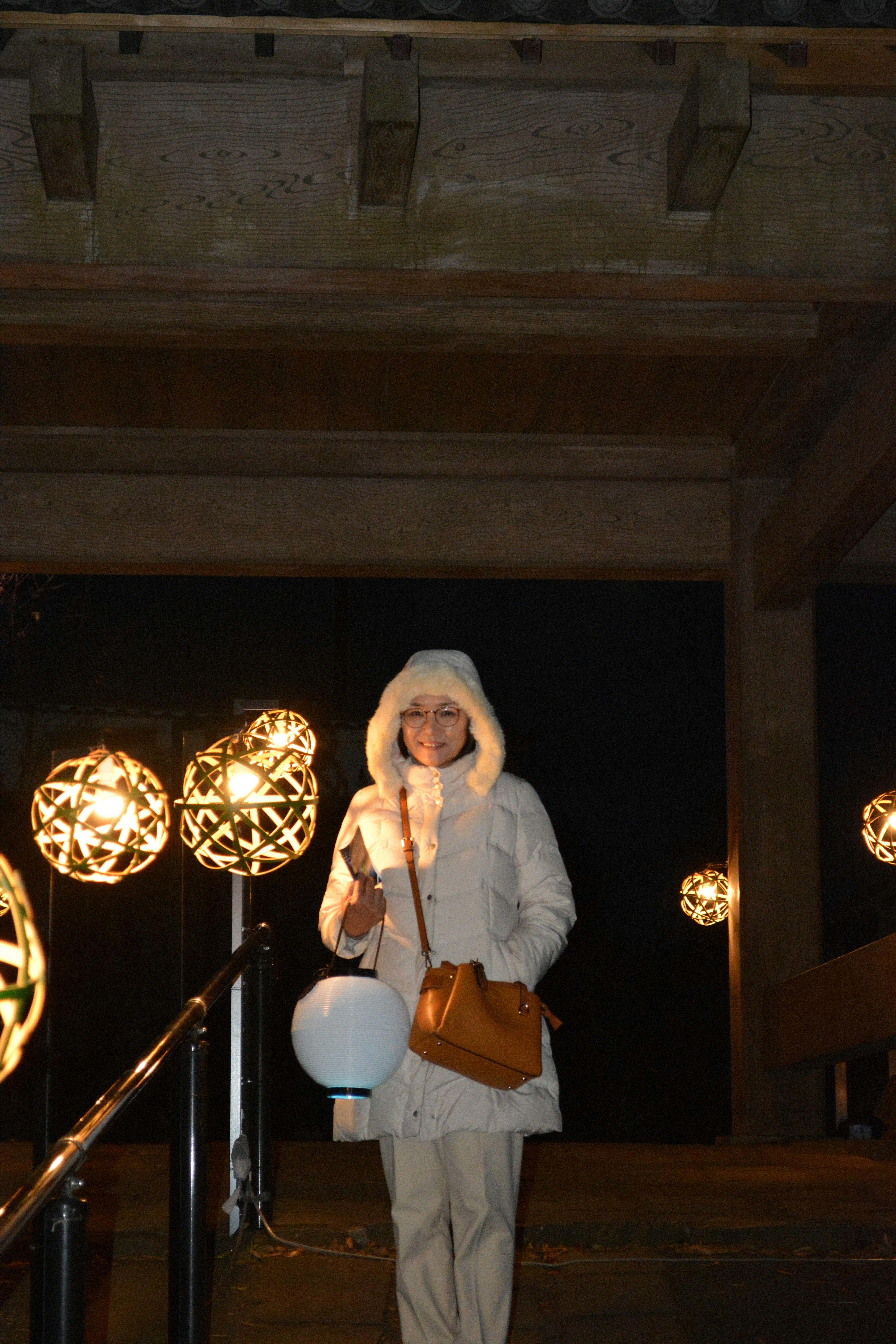 Femme en manteau à capuche blanc se tenant sous des lumières décoratives la nuit