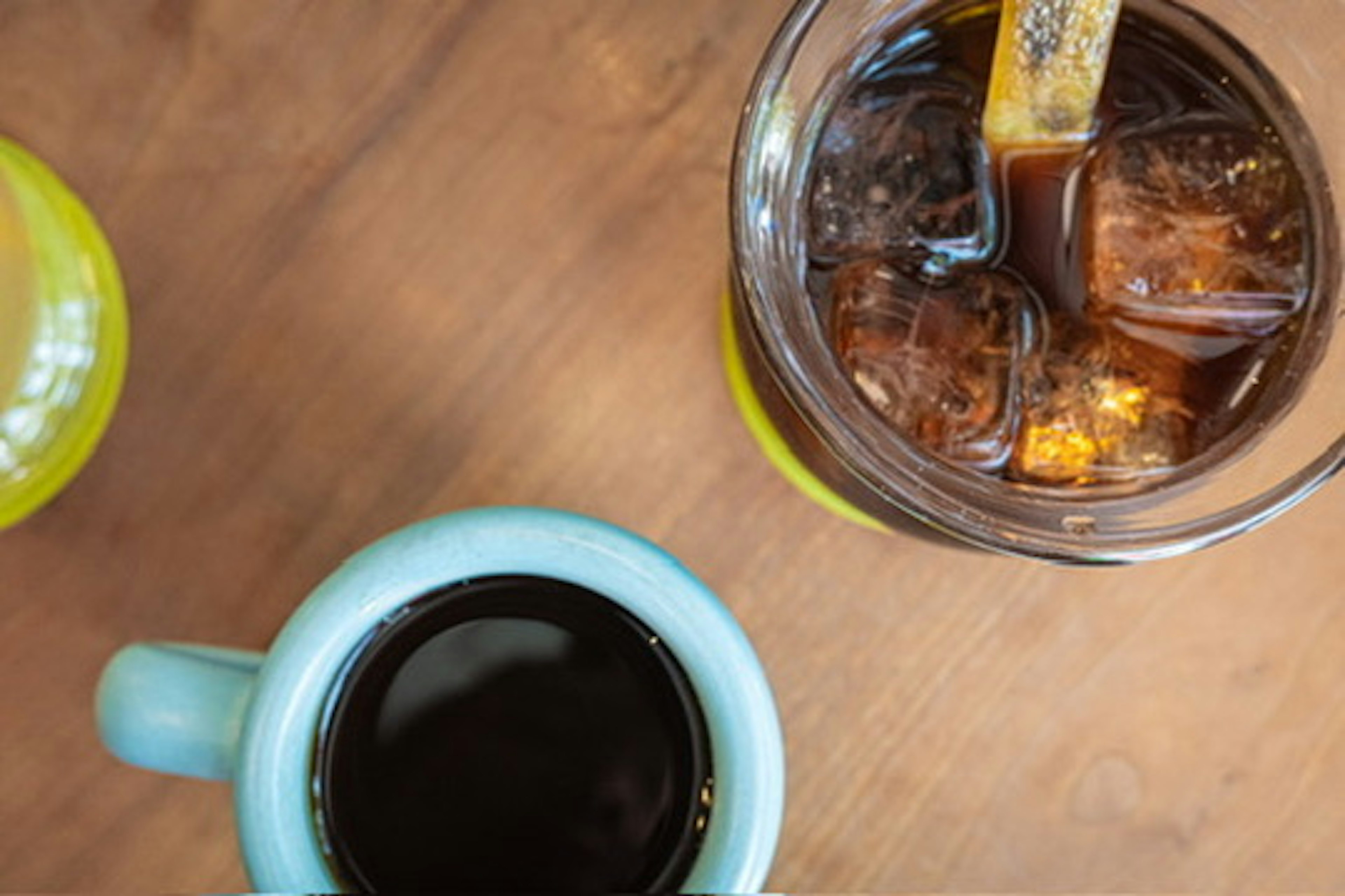 A blue coffee cup next to a glass of iced drink on a wooden table