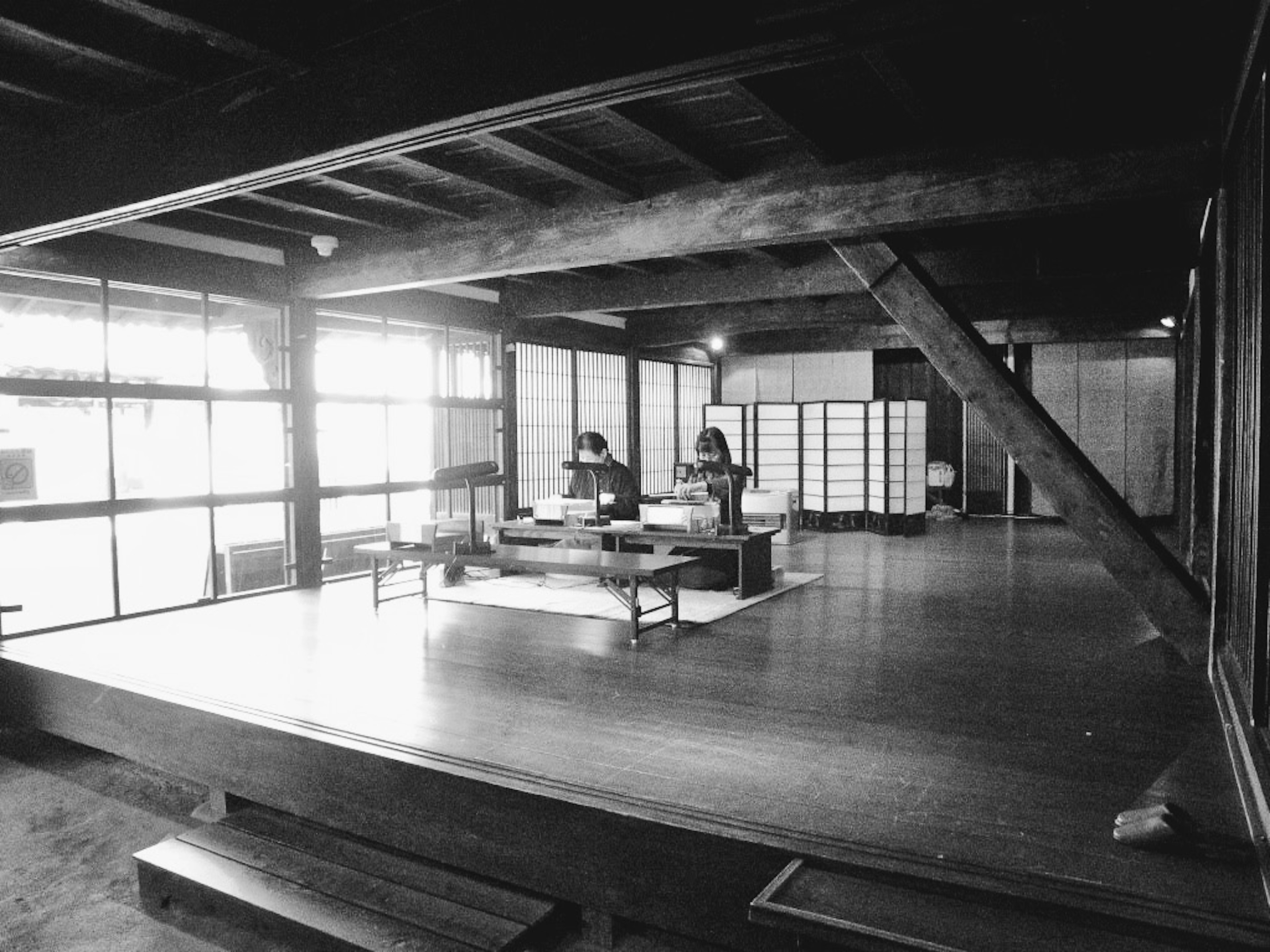 Traditionelles japanisches Zimmerinterieur mit Holzbalken und großen Fenstern, zwei Personen, die an einem Tisch arbeiten