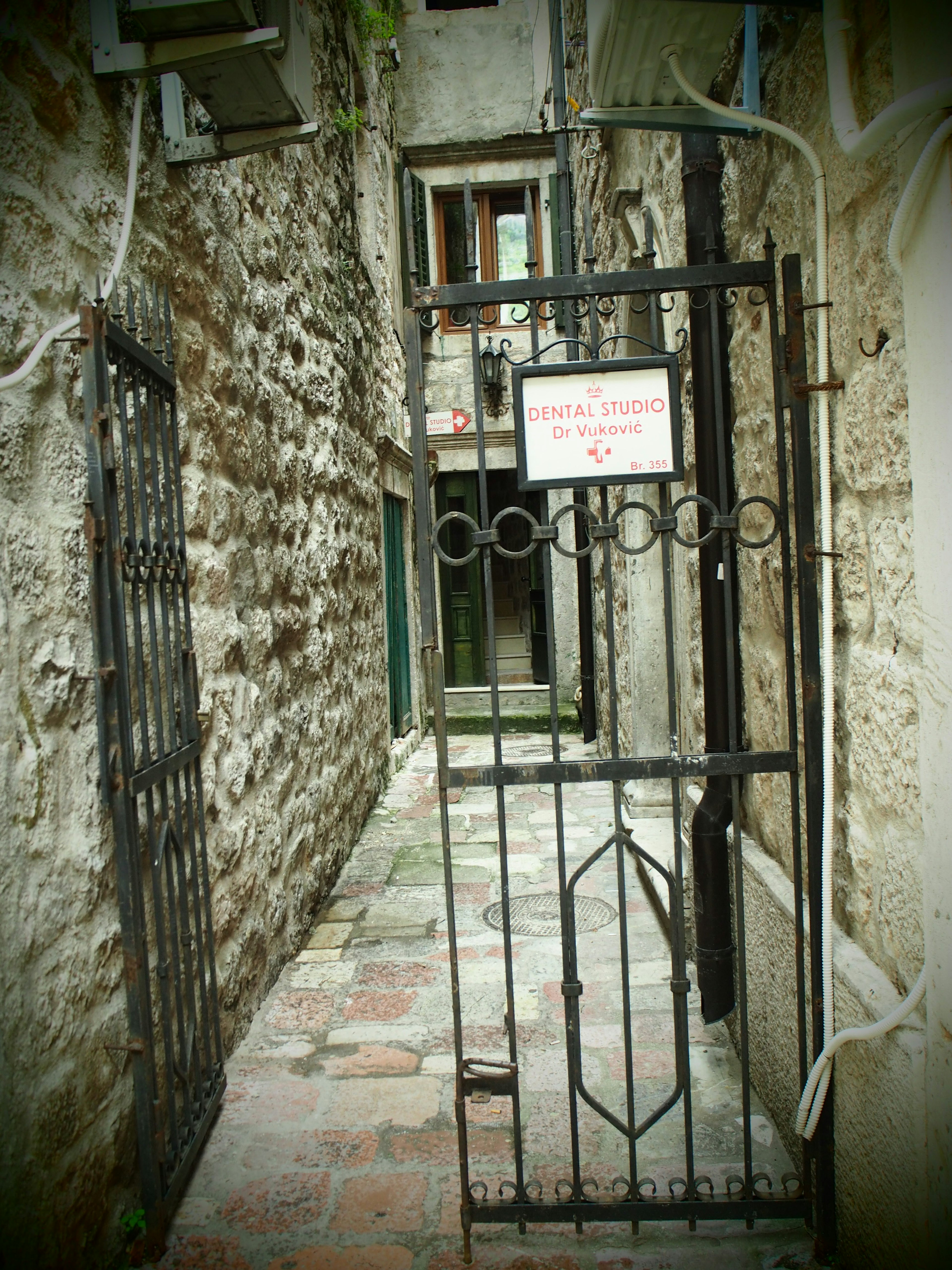 Narrow stone alley featuring a black iron gate and a sign