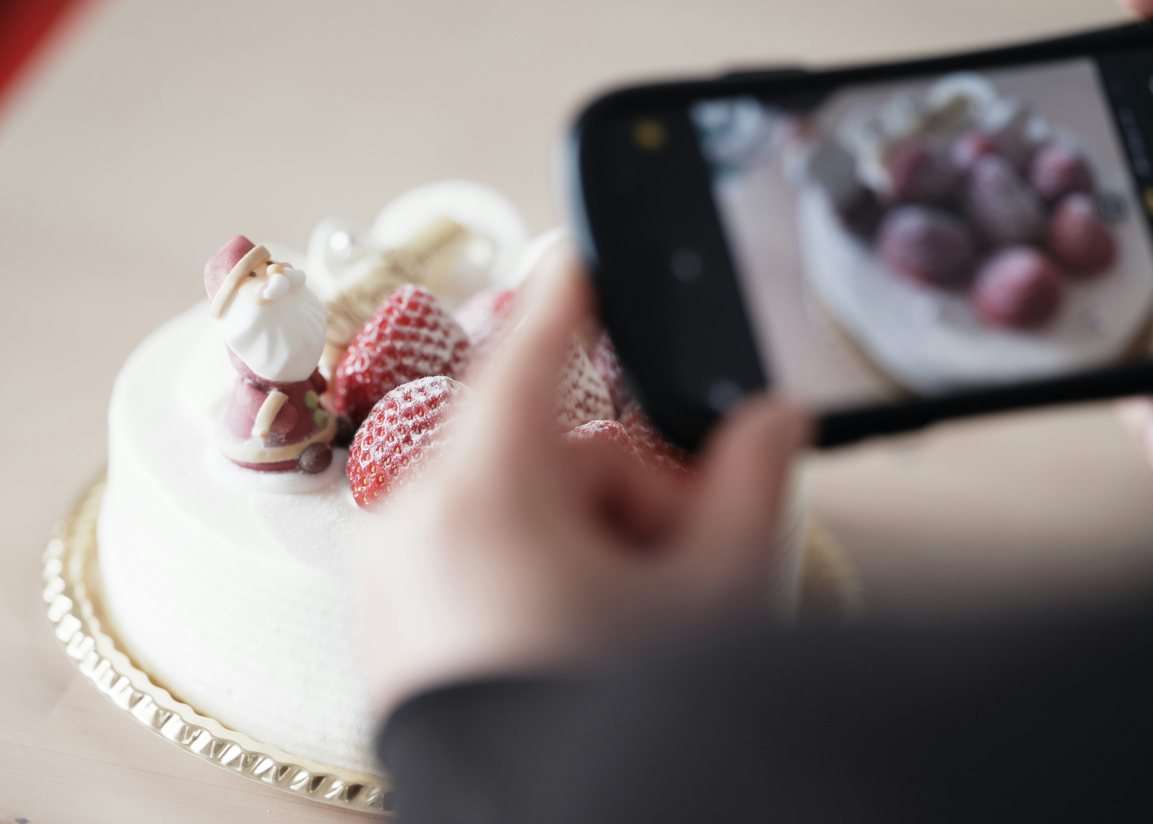 ケーキの上に飾られたイチゴと人形を撮影している手