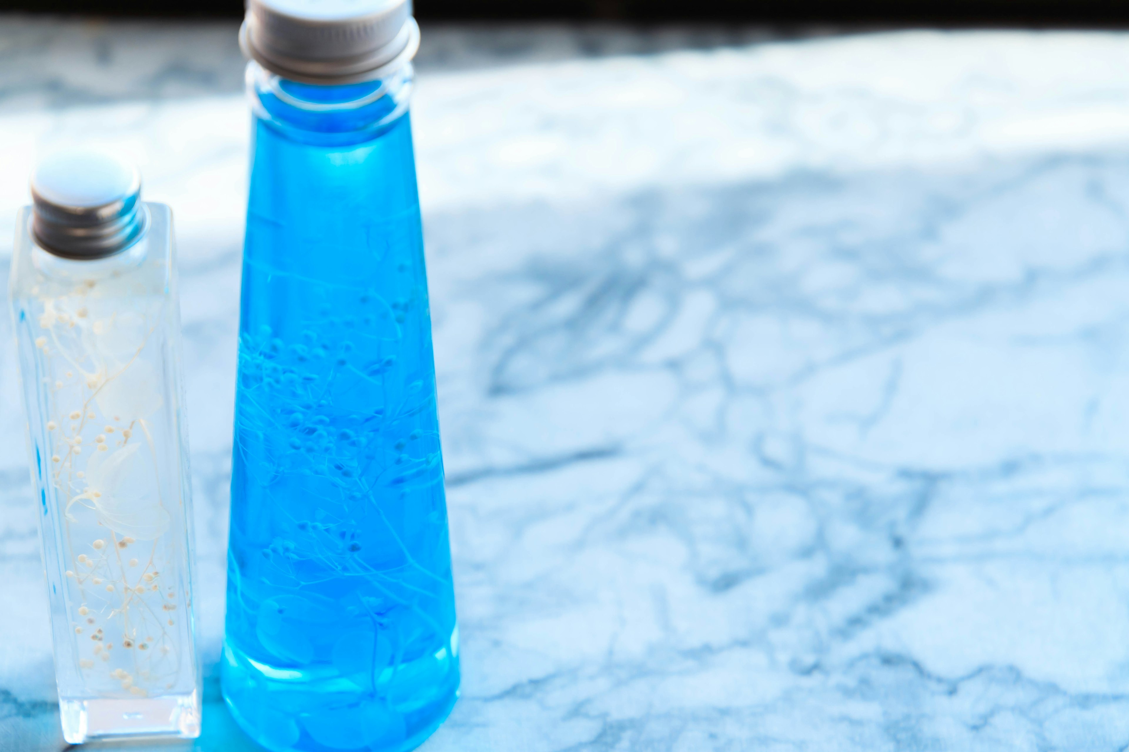 A blue liquid bottle and a clear bottle on a marble table