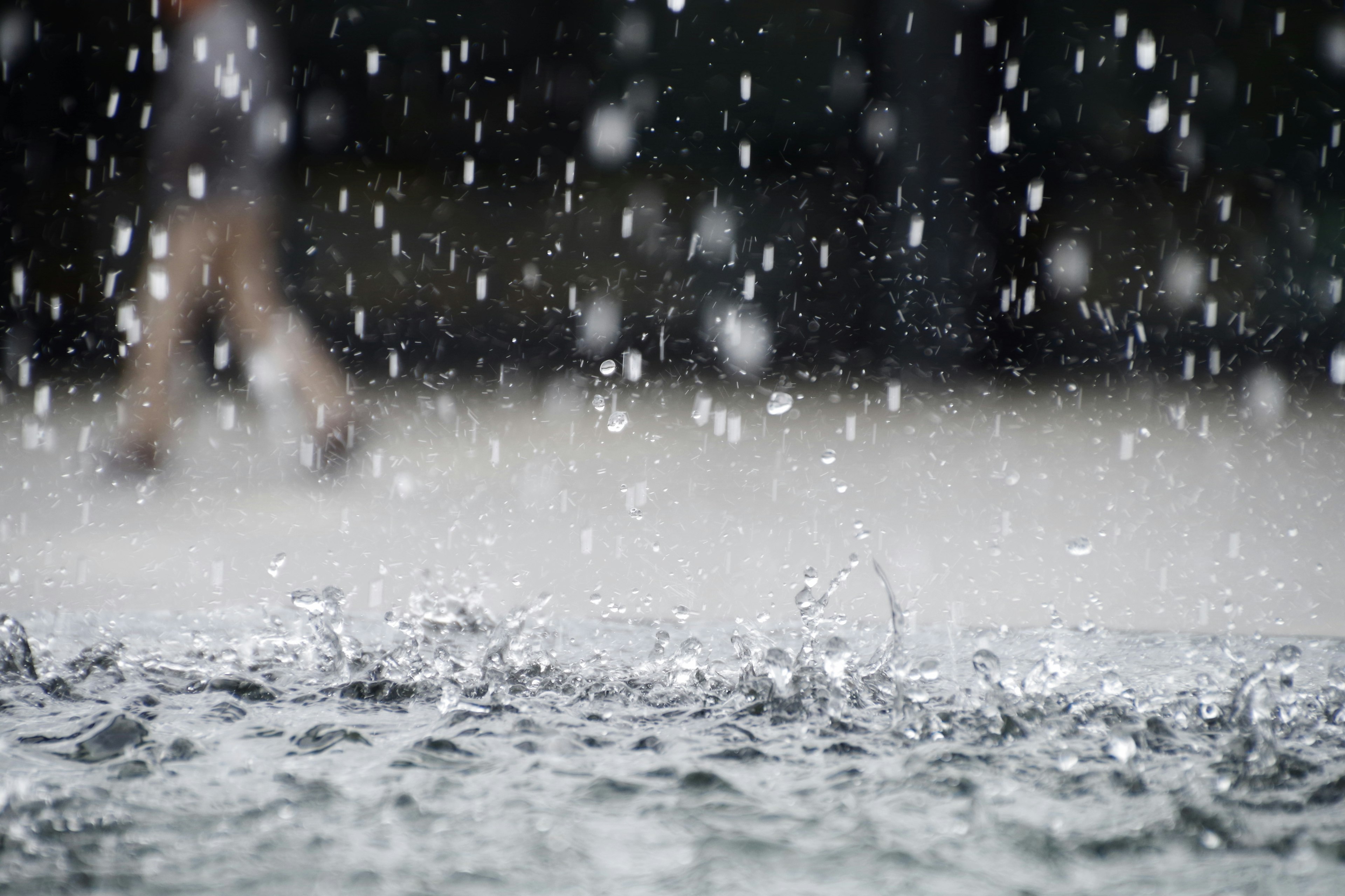 Raindrops falling on a water surface with a blurred figure in the background