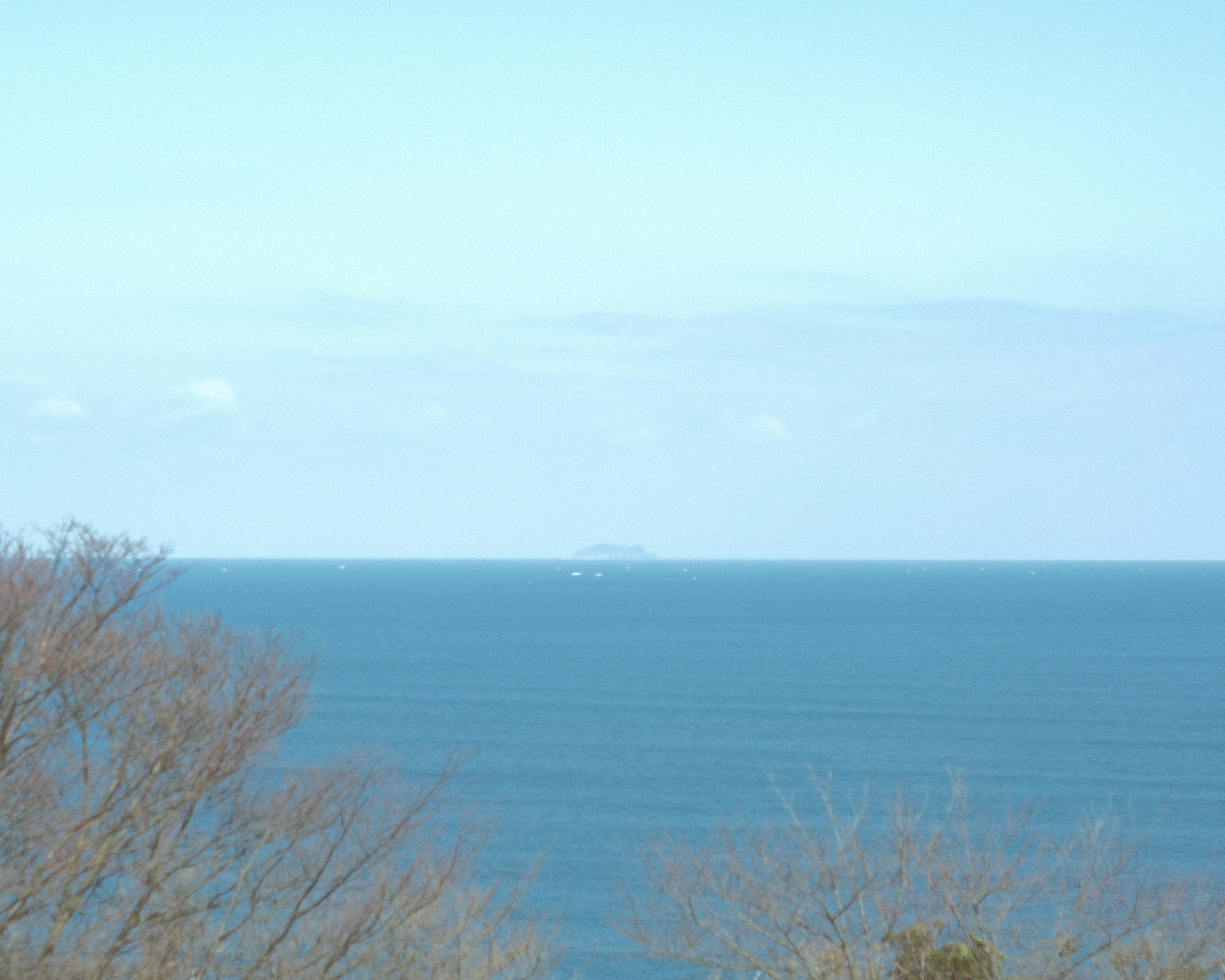 Vista del océano y el cielo azules con una pequeña isla a lo lejos