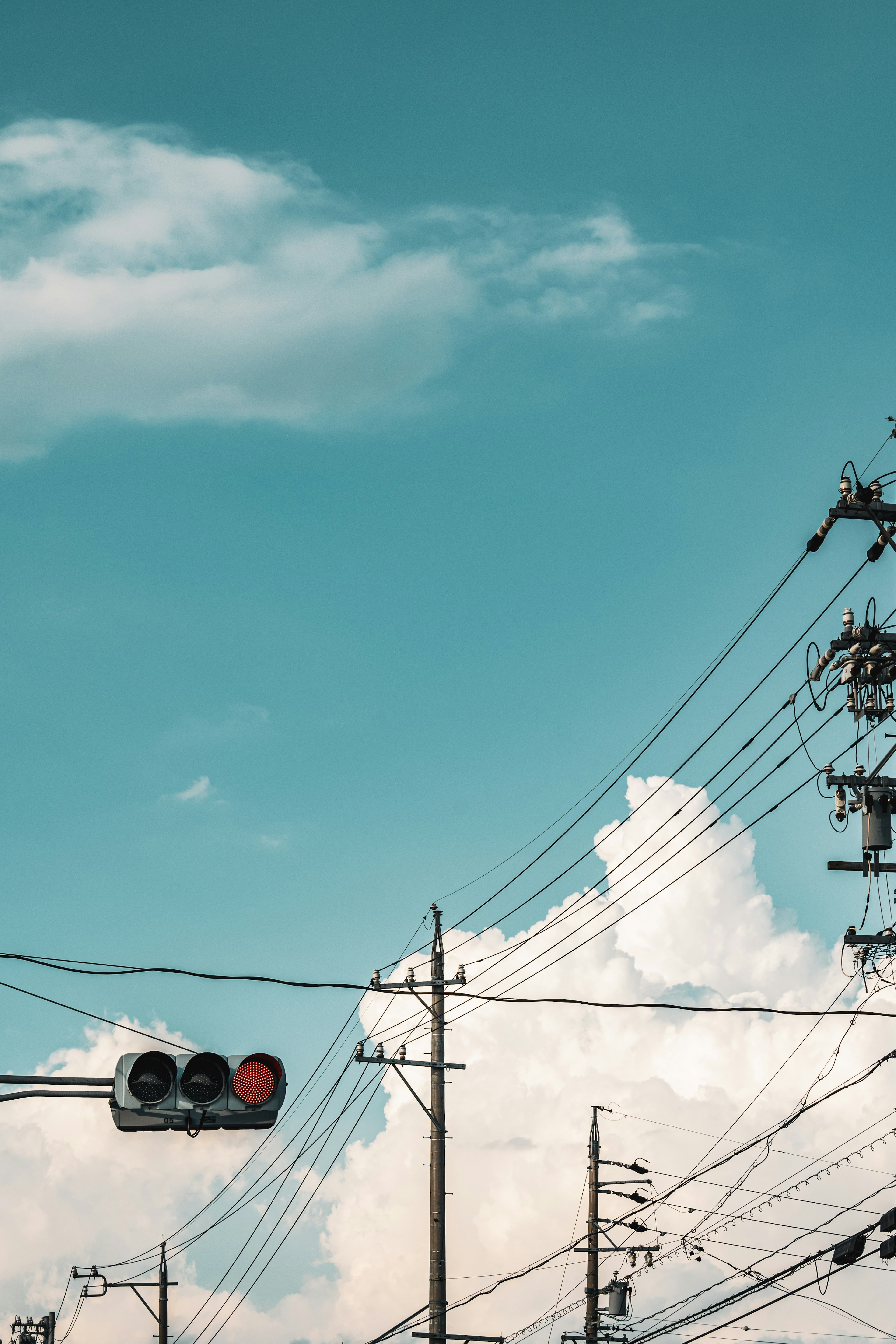 Railway signal and power lines against a blue sky with fluffy white clouds