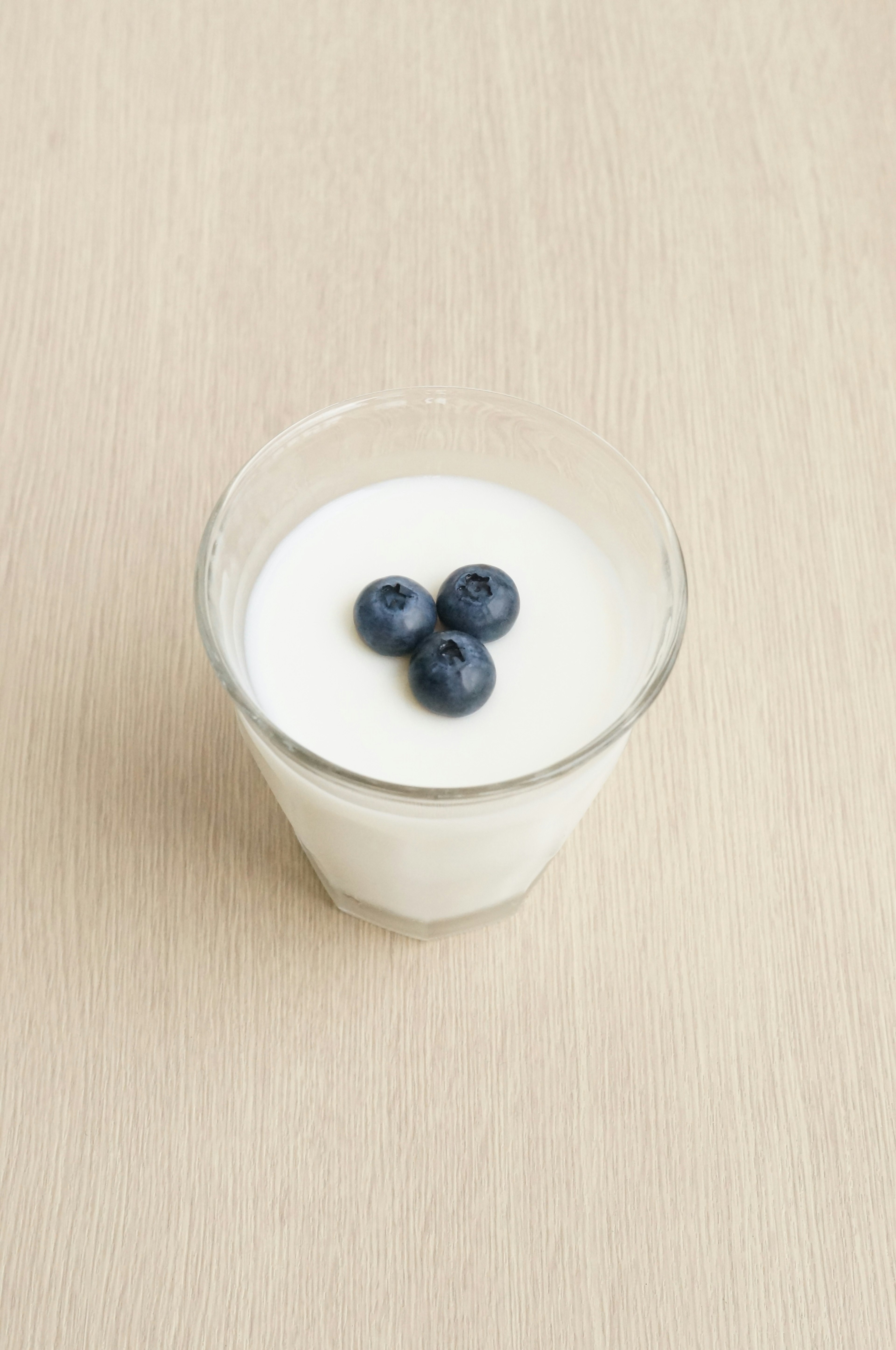 A glass cup of white yogurt topped with three blueberries