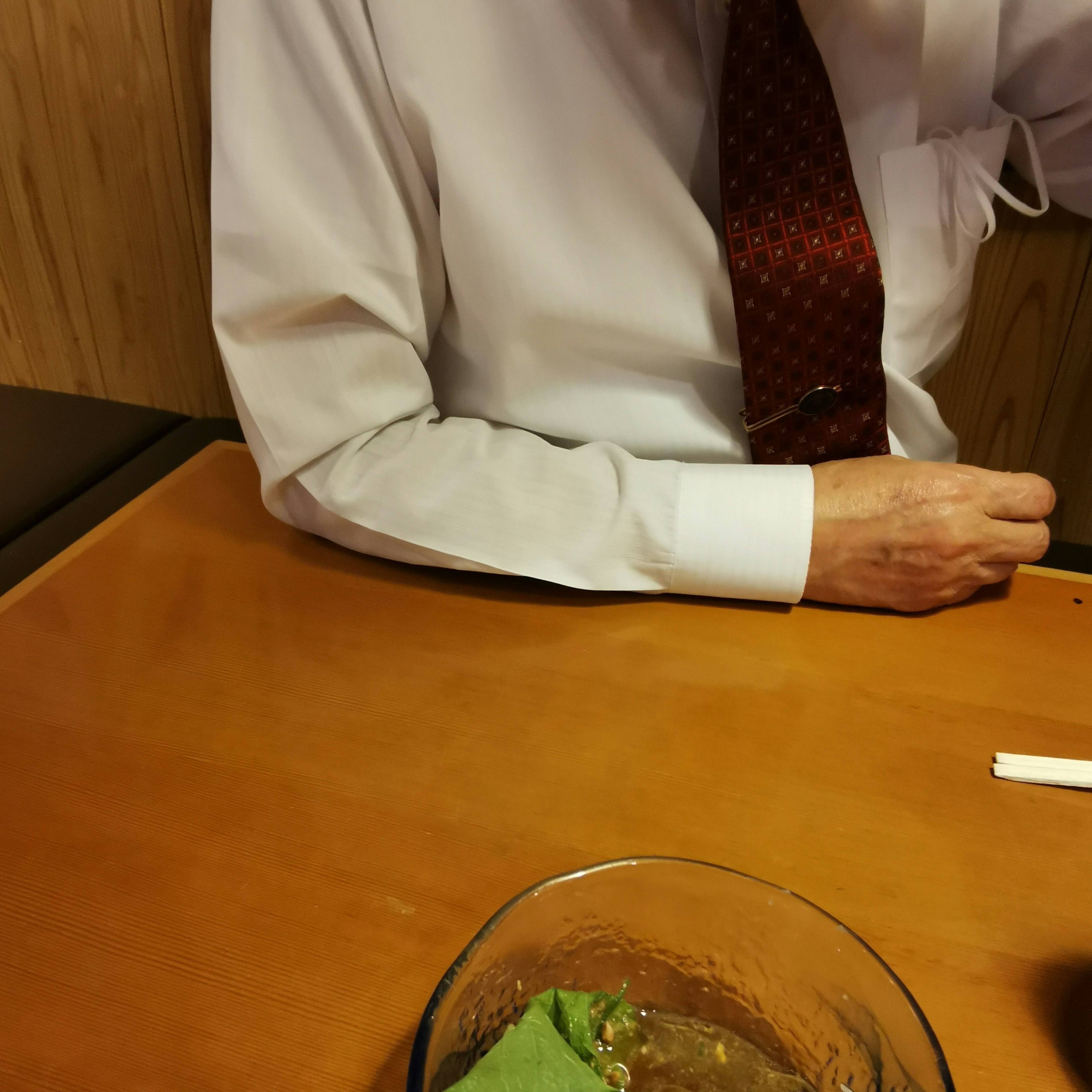 A man's arm in a white shirt and red tie is visible next to a dish on the table