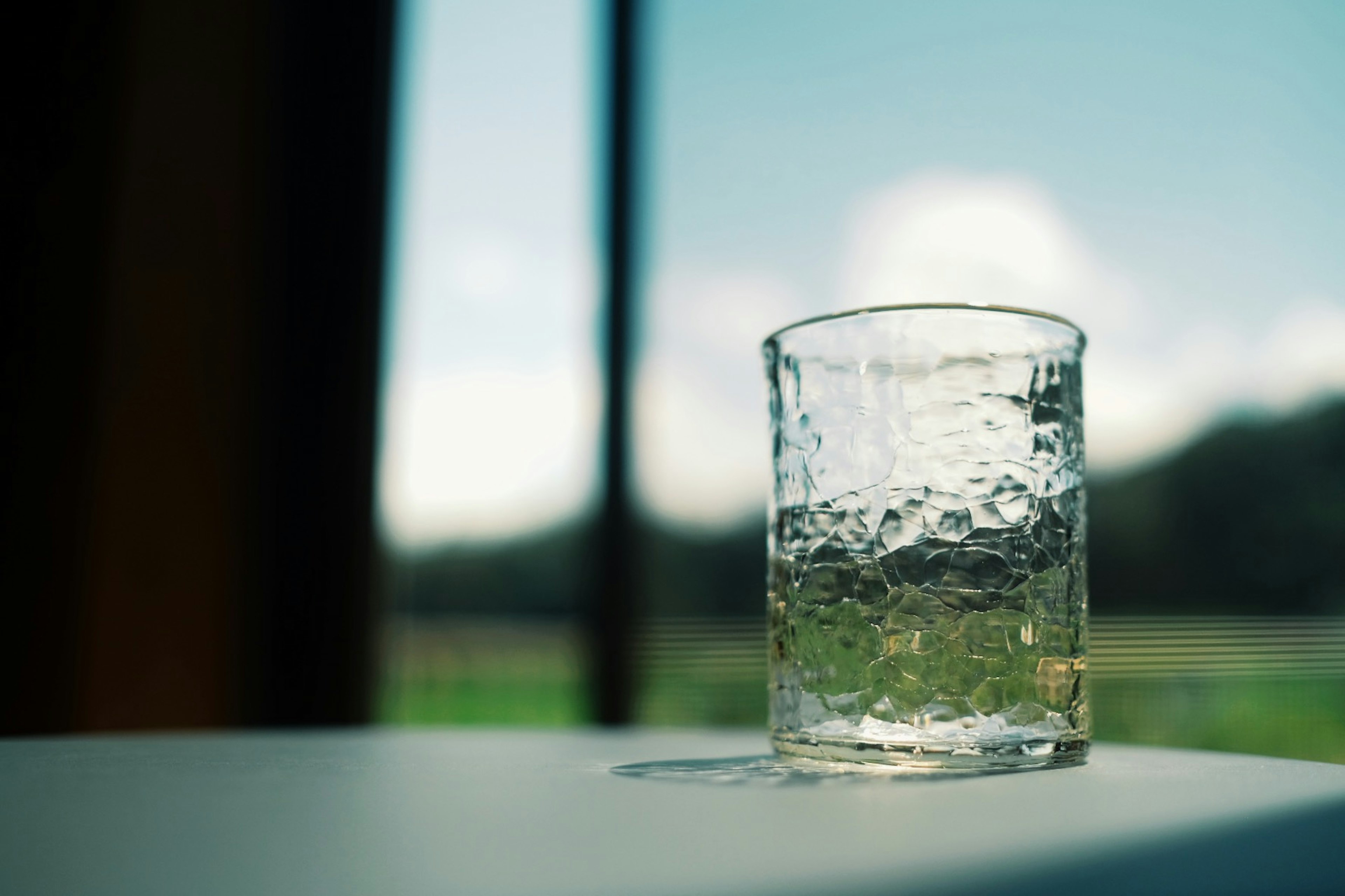 Close-up of a clear glass with water background features blue sky and green landscape